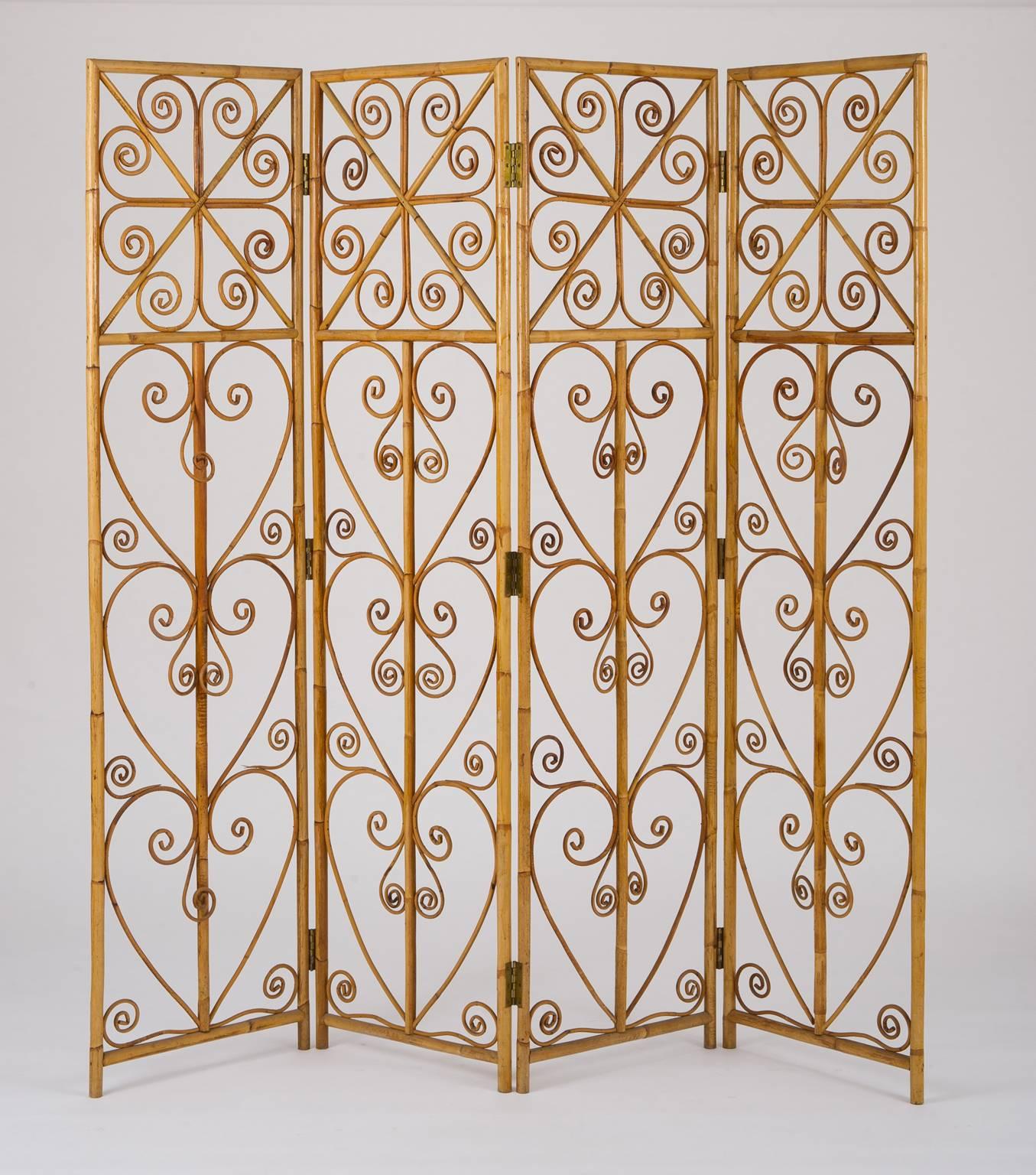 A large four-leaf bamboo and rattan screen or room divider, the bamboo frame with brass hinges and the screens adorned with various rattan scrolls,
France, circa 1950.