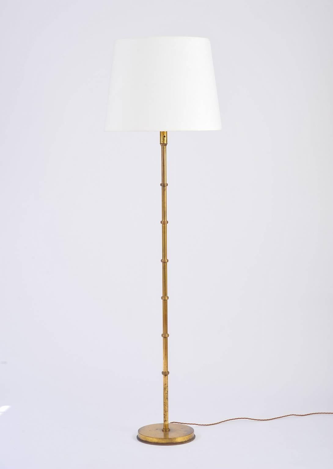 A brass floor lamp, the stylized bamboo stem on a stepped circular base and with a bespoke ivory fabric tapered shade.
France, circa 1950.