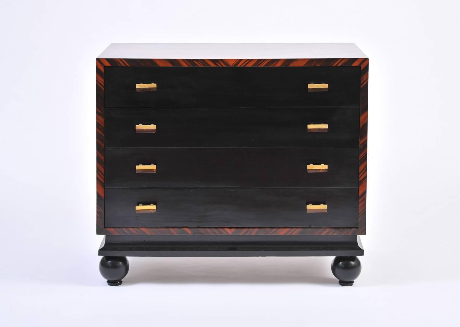 An Art Deco Macassar ebony and black lacquer four-drawer commode, each drawer adorned with brass and faux tortoiseshell bakelite handles, internally lacquered in coral, on solid ball feet,
Italy, circa 1935.
