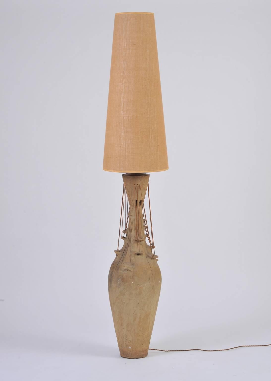 A monumental and unique studio pottery lamp, the imposing terracotta urn shaped base incorporating patinated ropes, supporting a large conical hessian shade,
England, circa 1960.