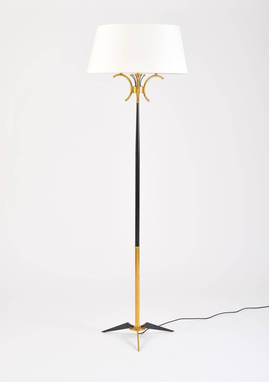 A brass and black enameled iron floor lamp the tapered stem on a shaped tripod base, holding three lights adorned with pistil-like elements, the original shade recovered in a new ivory material, topped by brass finial.
France, circa 1950.