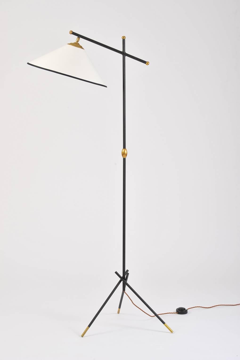 A brass and black enameled iron floor lamp, with its original shade recovered in new black edged ivory fabric, swiveling and orientation adjustable,
France, circa 1950.
