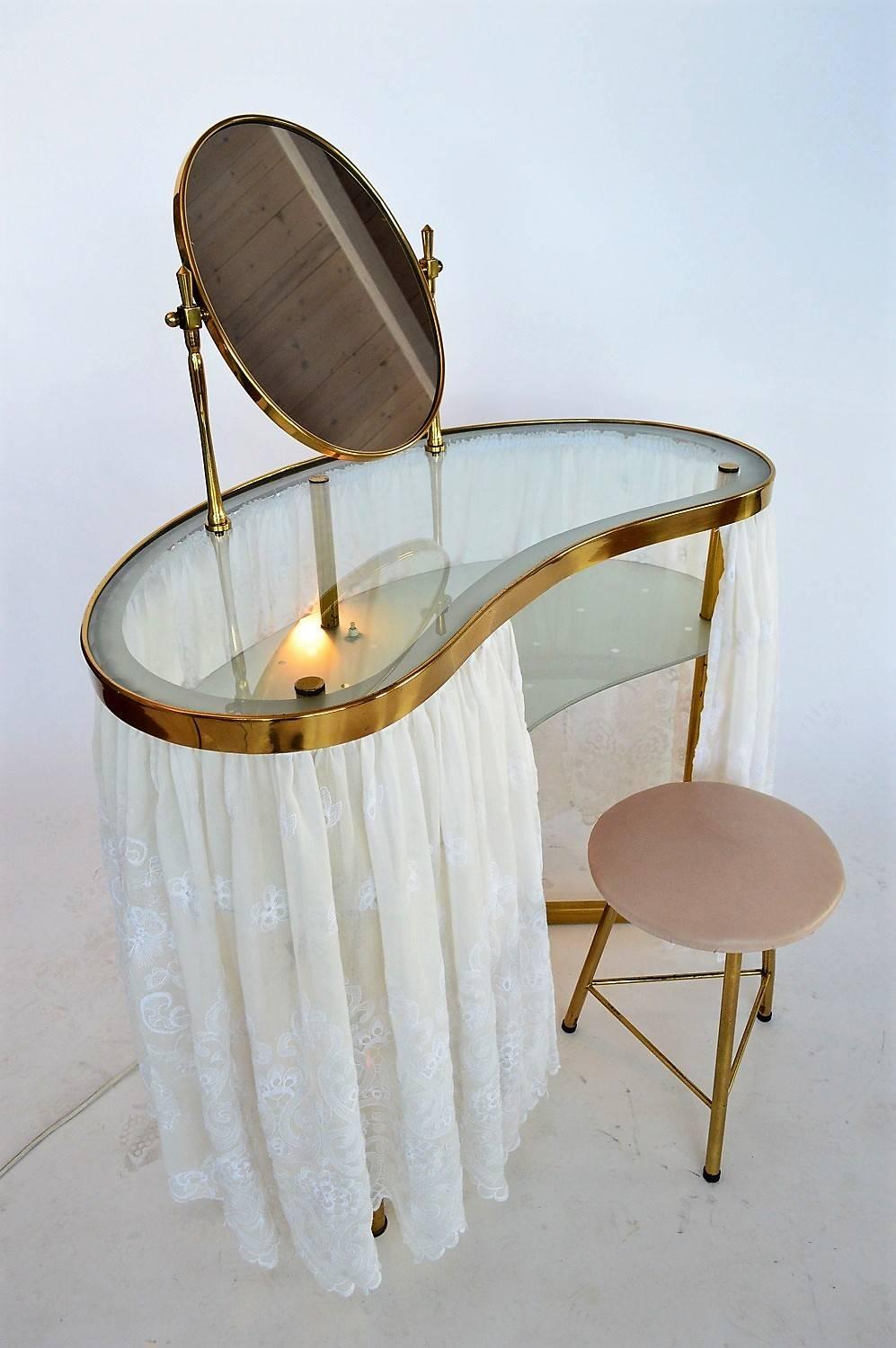 Gorgeous vanity or dressing table made of shiny brass, with glass shelf for deposing Creme and Parfum ecc.
Made in Italy in the 1950s
The table lights up underneath the glass shelf with a small bulb holder and on/off switch. The glass shelf is