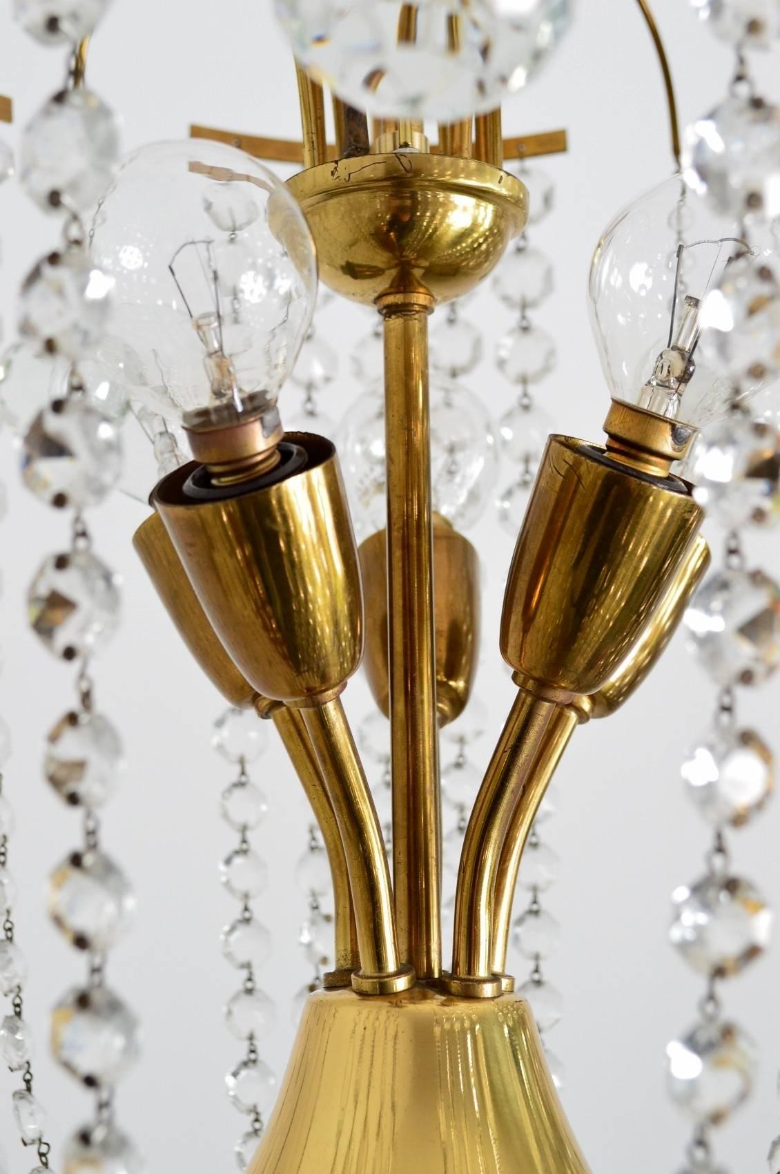 Un lampadario in ottone molto decorativo e originale con innumerevoli catene di cristallo lucido e sei sfere di cristallo pendenti intorno.
Realizzato in Austria negli anni '50, articolo nuovo di zecca.
L'intera struttura della lampada e la barra a