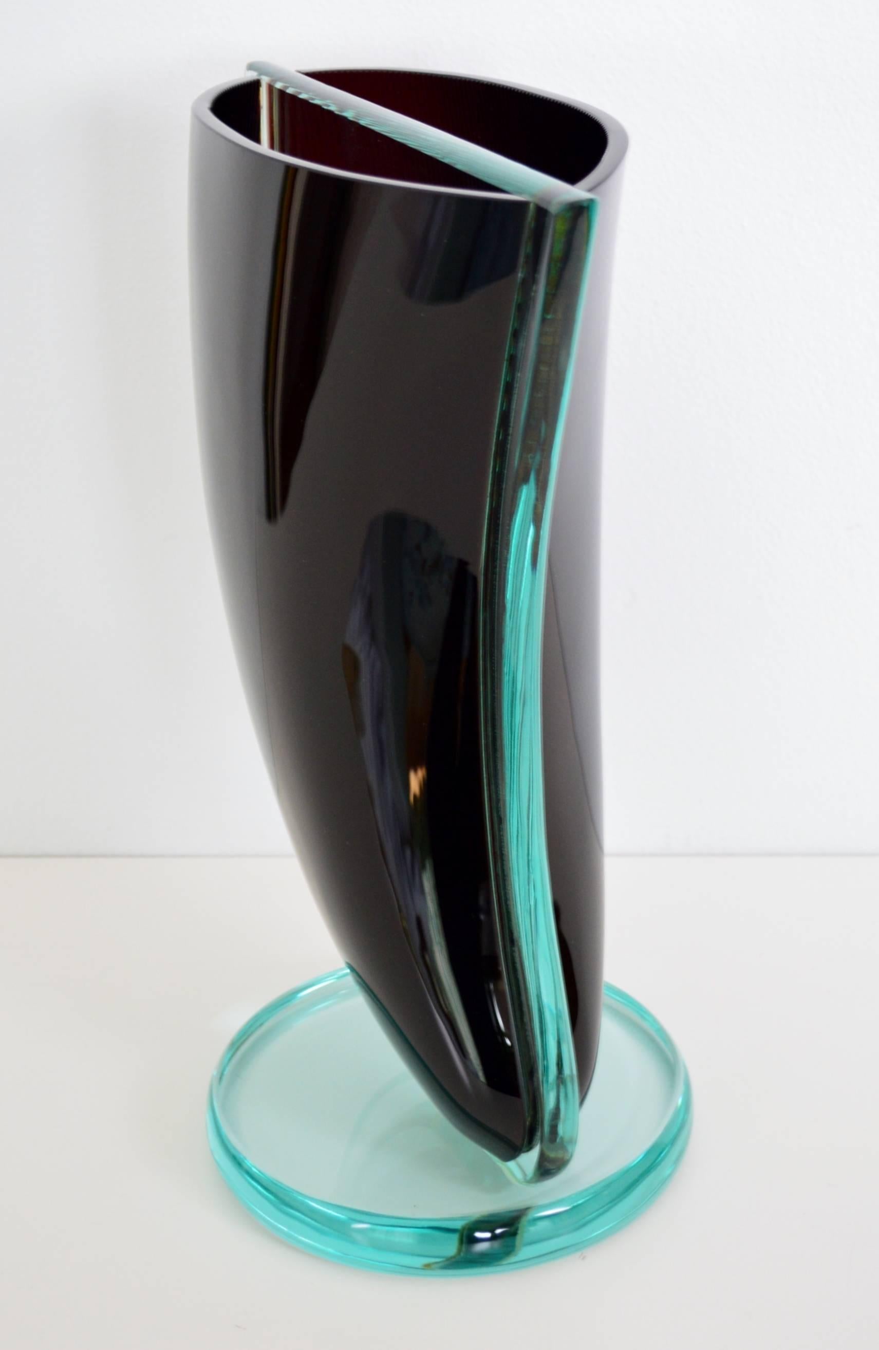 A very large glass sculpture vase made of dark red and transparent glass. The dark red almost goes into the black.
Attributed to Murano Glass from the 1960/1970s.
The shape of the vase seems to be a turned sail and is divided in the middle with a