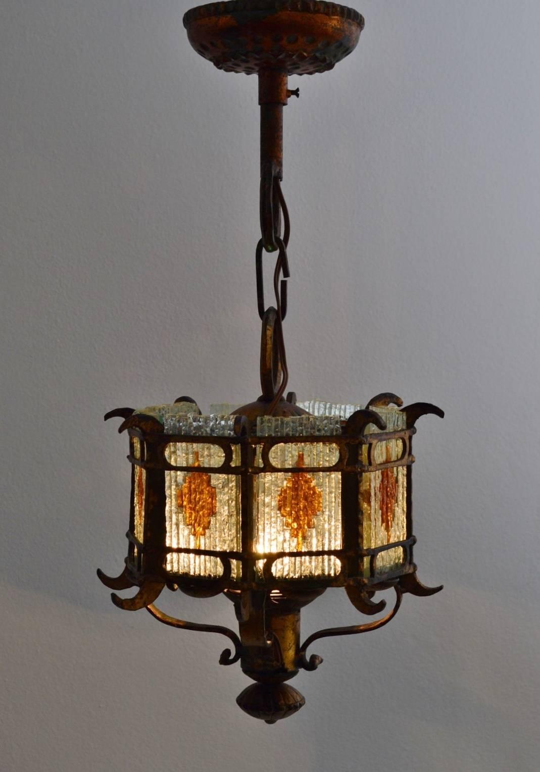 This heavy lantern in Brutalist style has been made in the 1960s in limited edition by a Master blacksmith.
The lamp's frame is made of heavy wrought iron, which has been hammered and gilt with effects in copper color.
It has eight pieces of cut