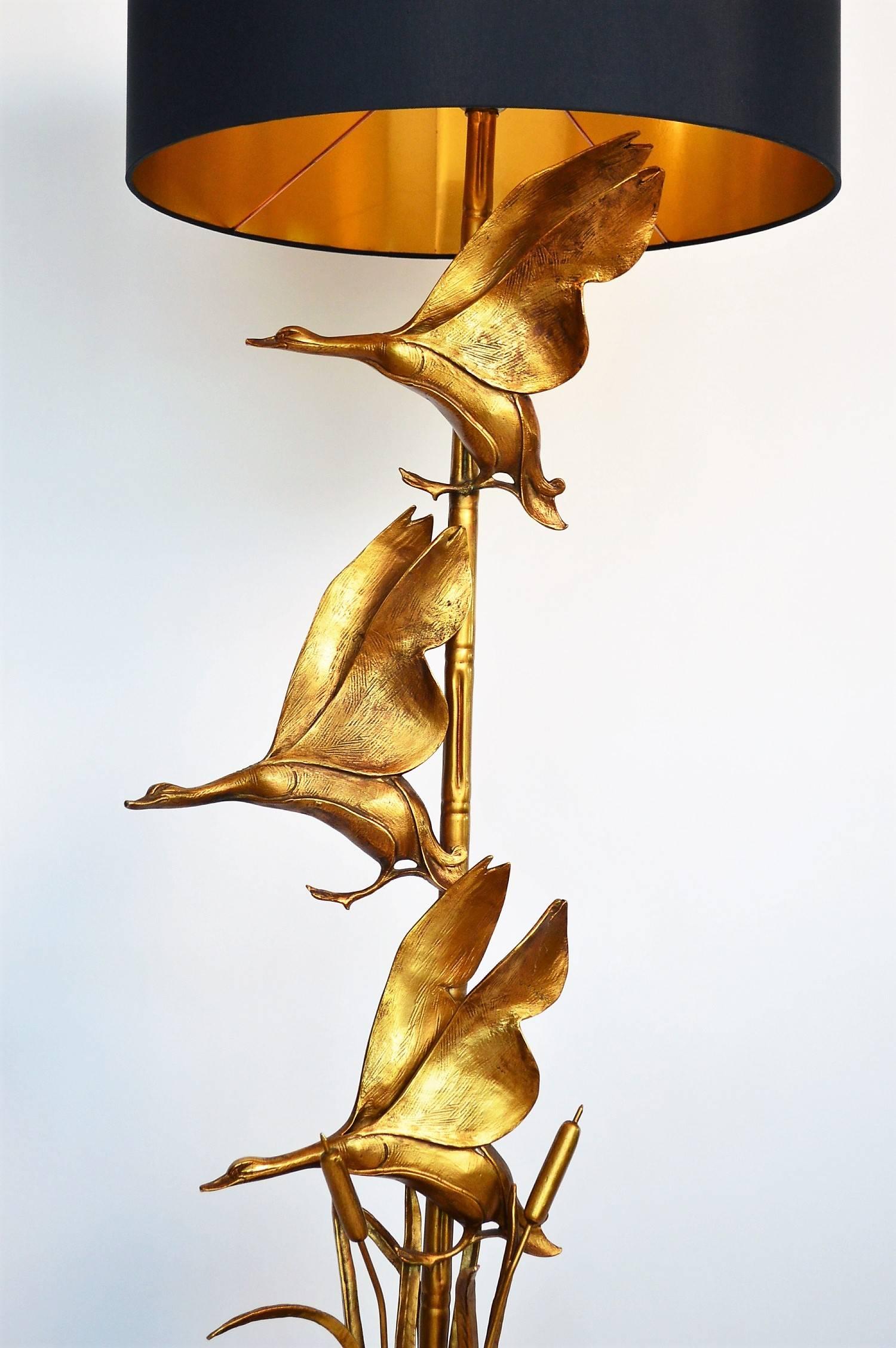 Extraordinary decorative floor lamp made of brass with black wooden pedestral.
The lamp body consists of a brass tube in bamboo optics, which is mounted on the pedestal. On this tube are three ducks (in brass) in flight. Among the ducks reed and