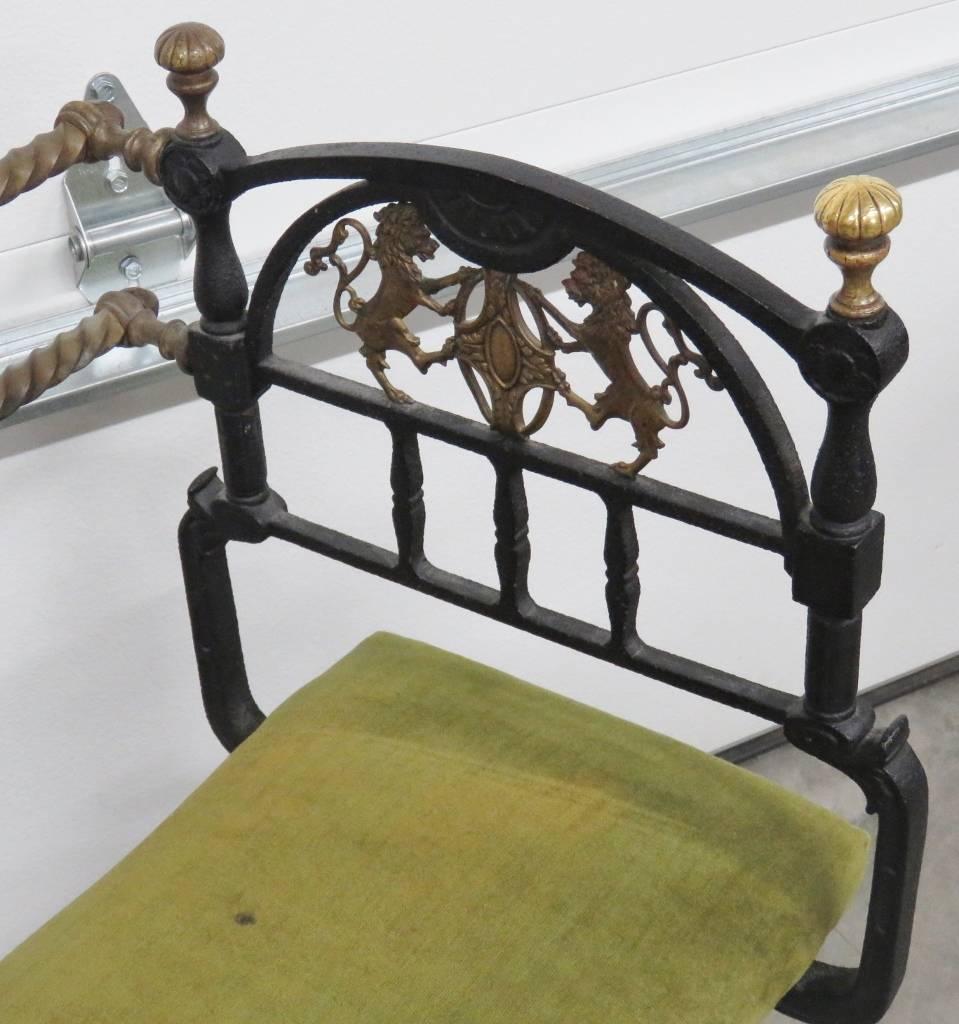 Black Iron with gold painted highlights. Green upholstered cushion. Brass knobs and decoration.