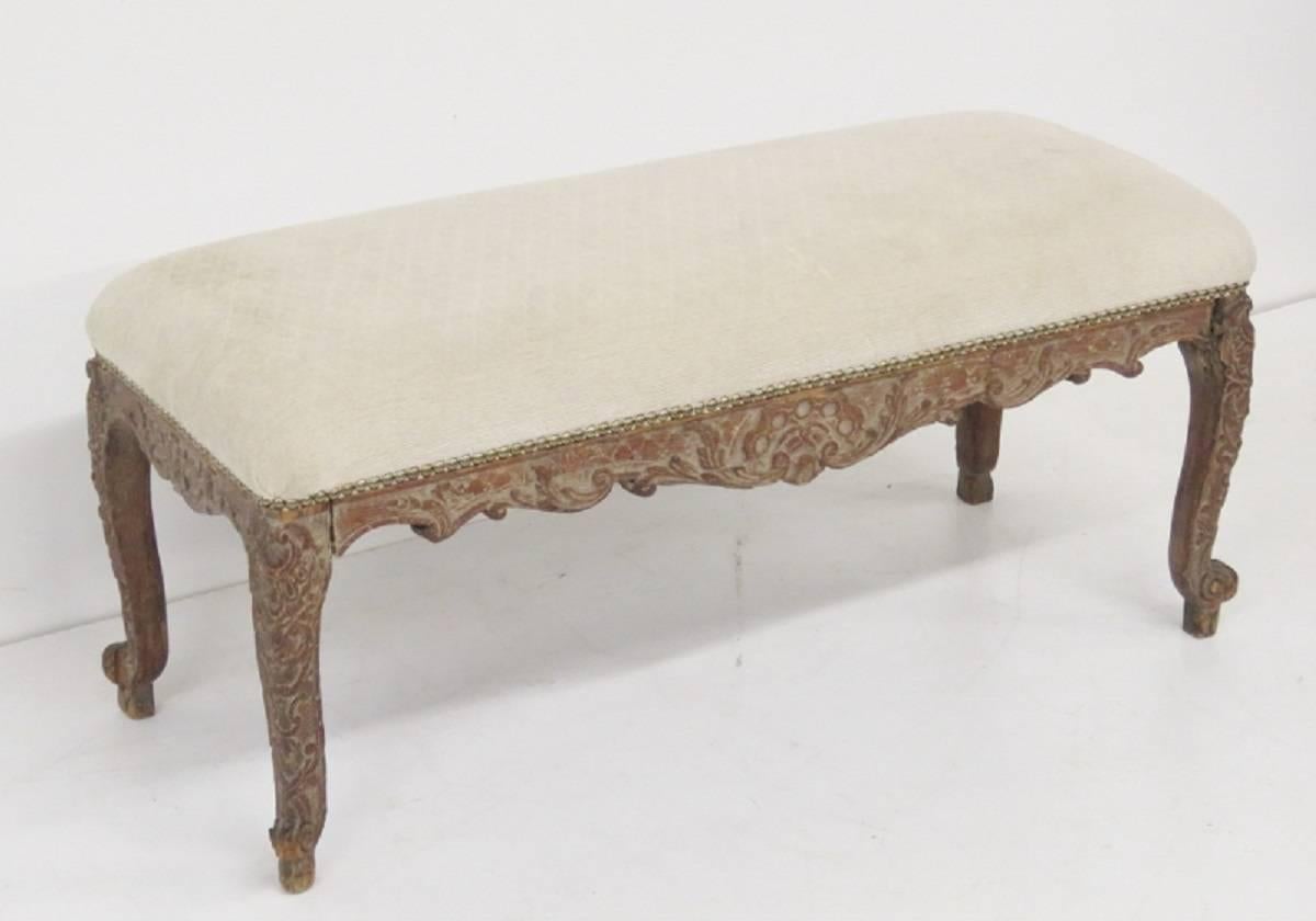 Bench has an intricately carved base with cream upholstered cushion.