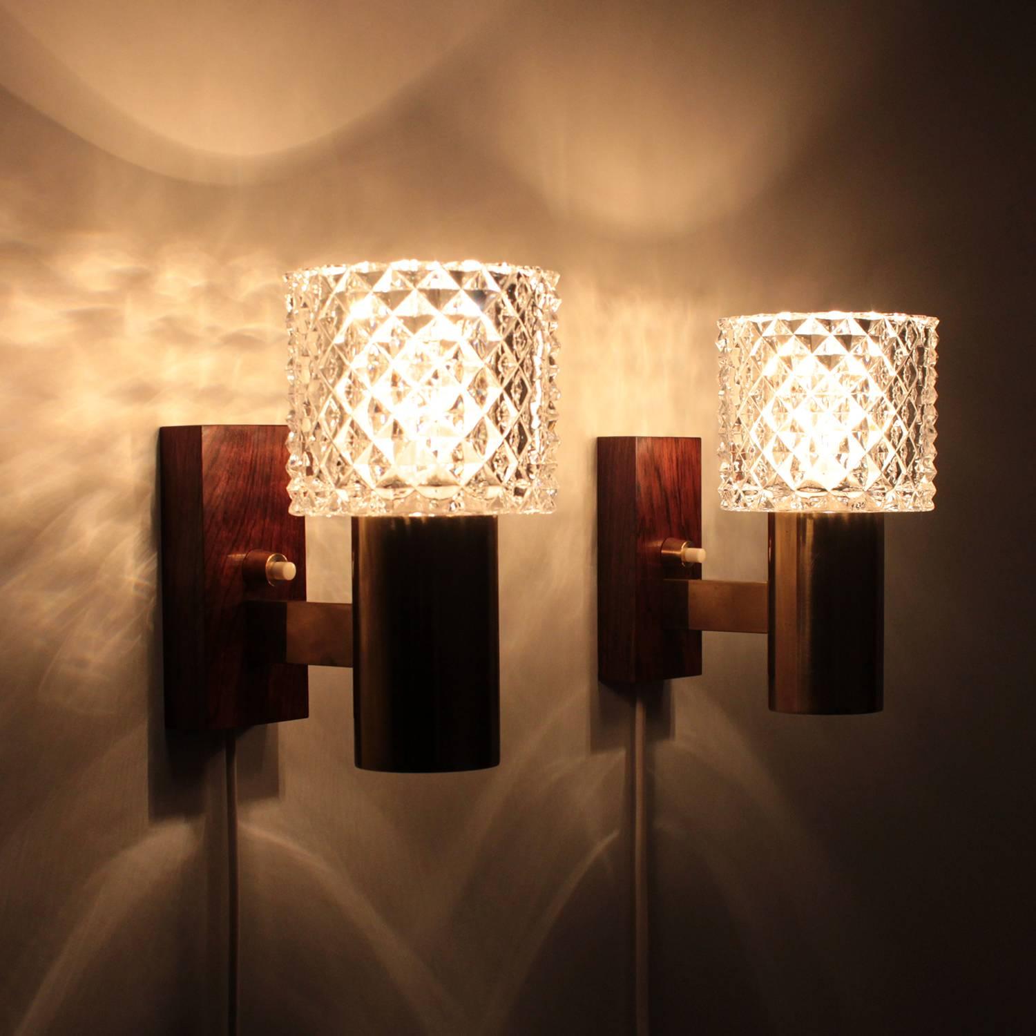 Crystal glass and rosewood pair of wall sconces from the 1960s by unknown Scandinavian producer - very stylish crystal wall lights with brass and rosewood - in excellent vintage condition.

Each light is comprised of a thick crystal glass shade, a