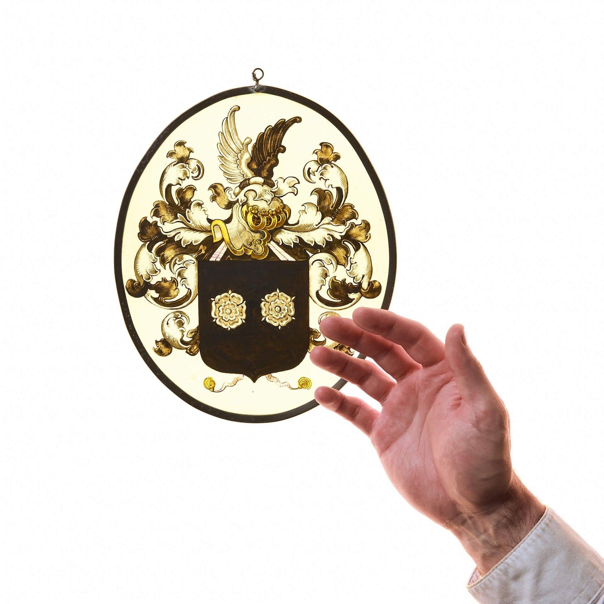 Vitrail ovale armorial allemand du 19e siècle.

Ce petit vitrail ovale représente un blason familial, composé d'un écu noir marqué de deux roses de Tudor, au-dessous d'un feuillage en volutes et d'un casque de chevalier surmonté des ailes noires et