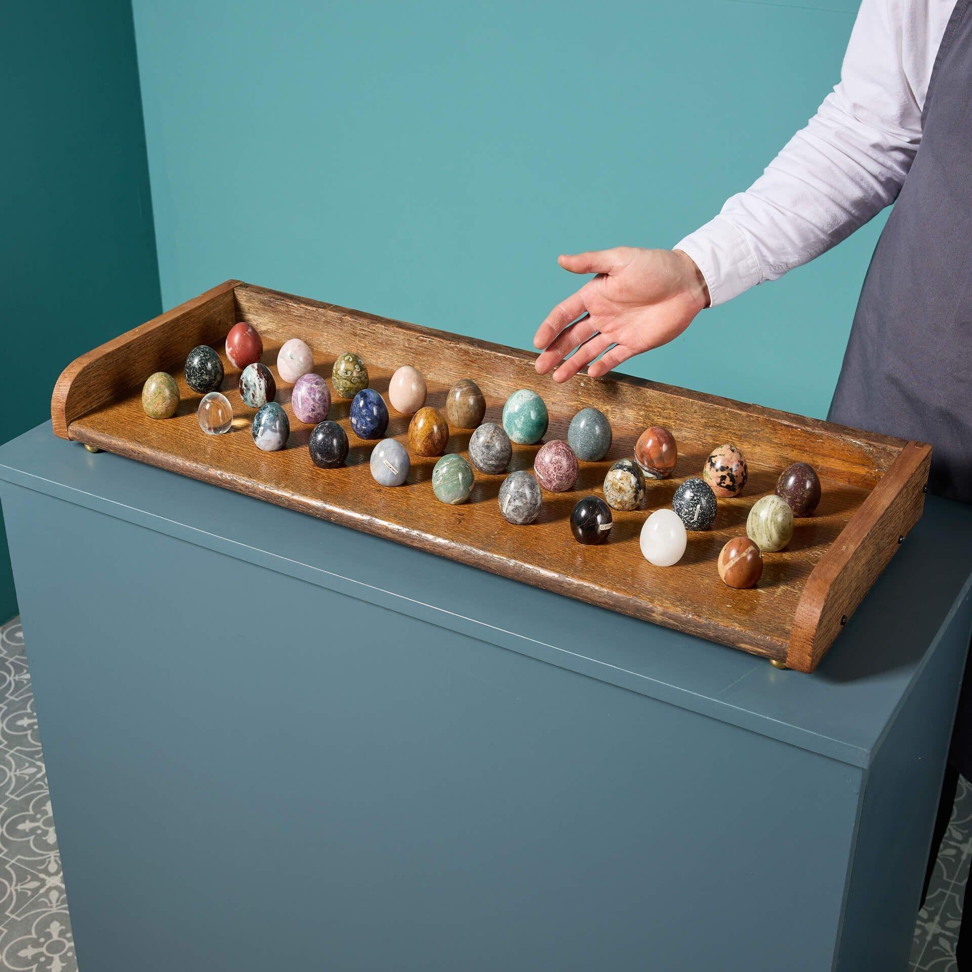 A collection of 30 polished specimen hardstone and marble eggs displaying a variety of minerals.
 
Displayed in an oak stand with round brass feet, these beautiful eggs include sodalite, mtorolite, jasper, fossil wood and basalt in various sizes