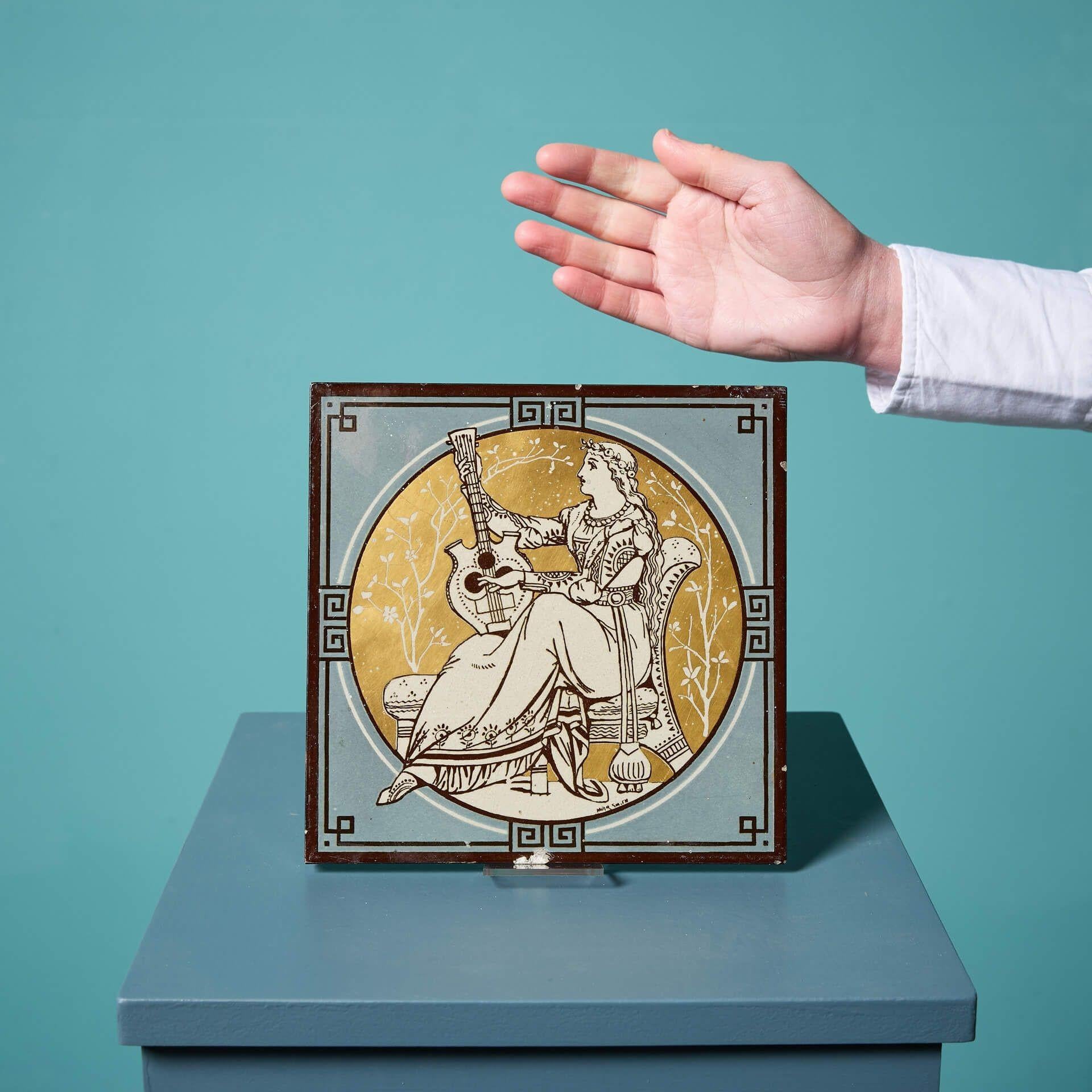 An antique late 19th century Minton tile from the series ‘Classical Figures with Musical Instruments’ by the artist John Moyr Smith.
 
This 8 inch tile depicts a noble woman in roman style dress playing a lyre in a neoclassical scene, hand painted