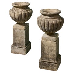 Paire d'urnes en pierre de composition, à godrons, patinées, posées sur des socles