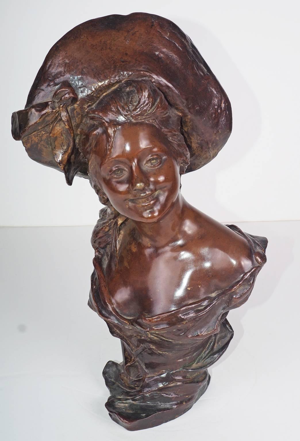 Bronze bust of a young woman wearing a hat.