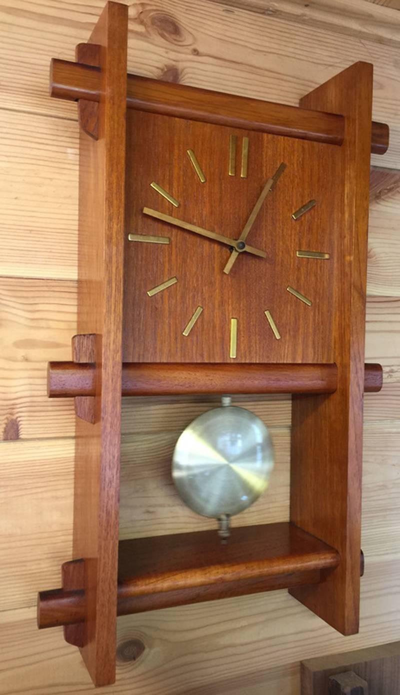Teak clock, which has a swinging pendulum and is battery operated (single aa battery) in perfect working condition. Shown on a wall in the photos, it can also be freestanding.