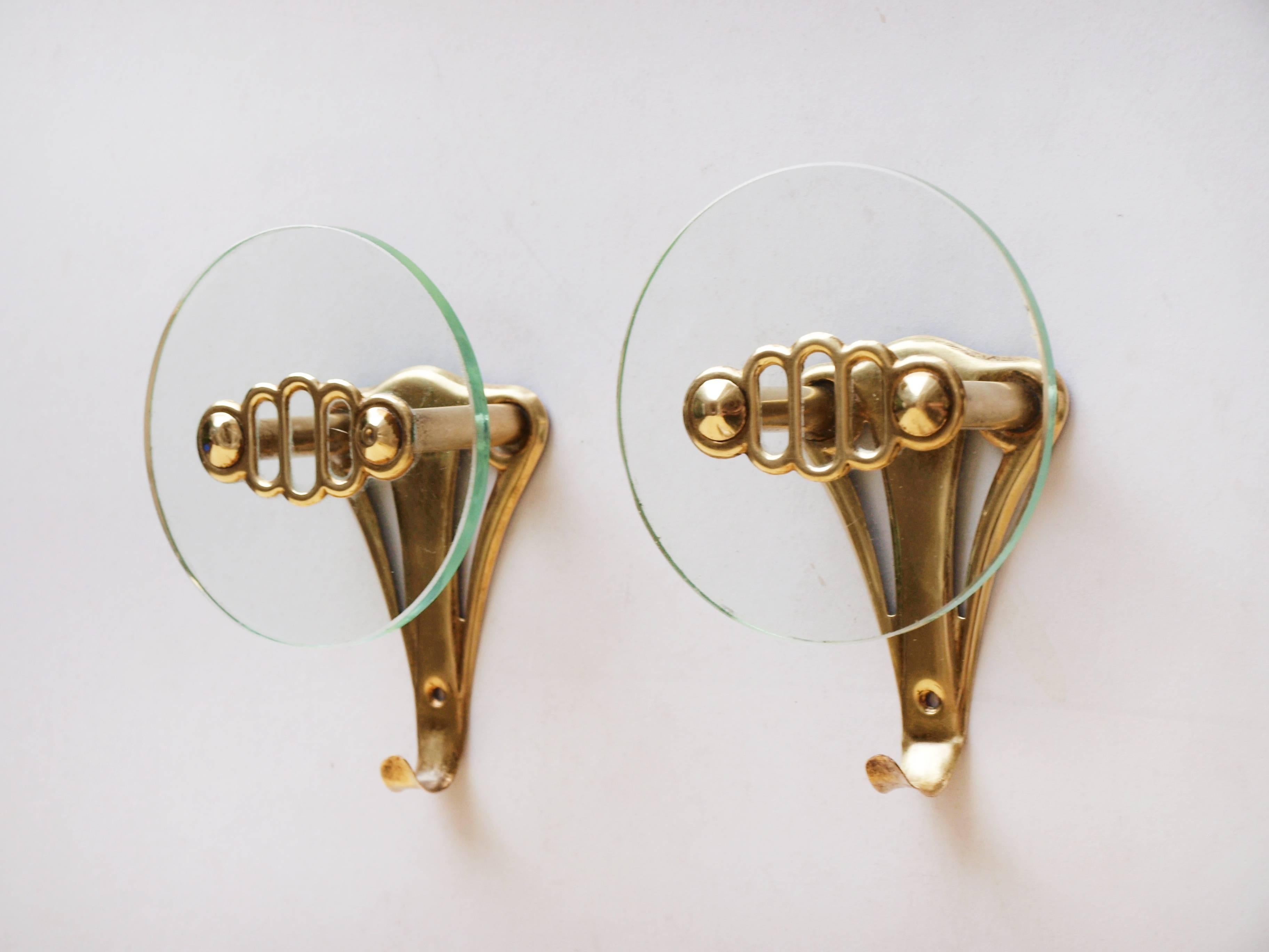 A pair of fan shaped Italian brass and glass wall-mounted coat hooks designed, circa 1950, with an ornamental circular glass disc and brass detailing.

 