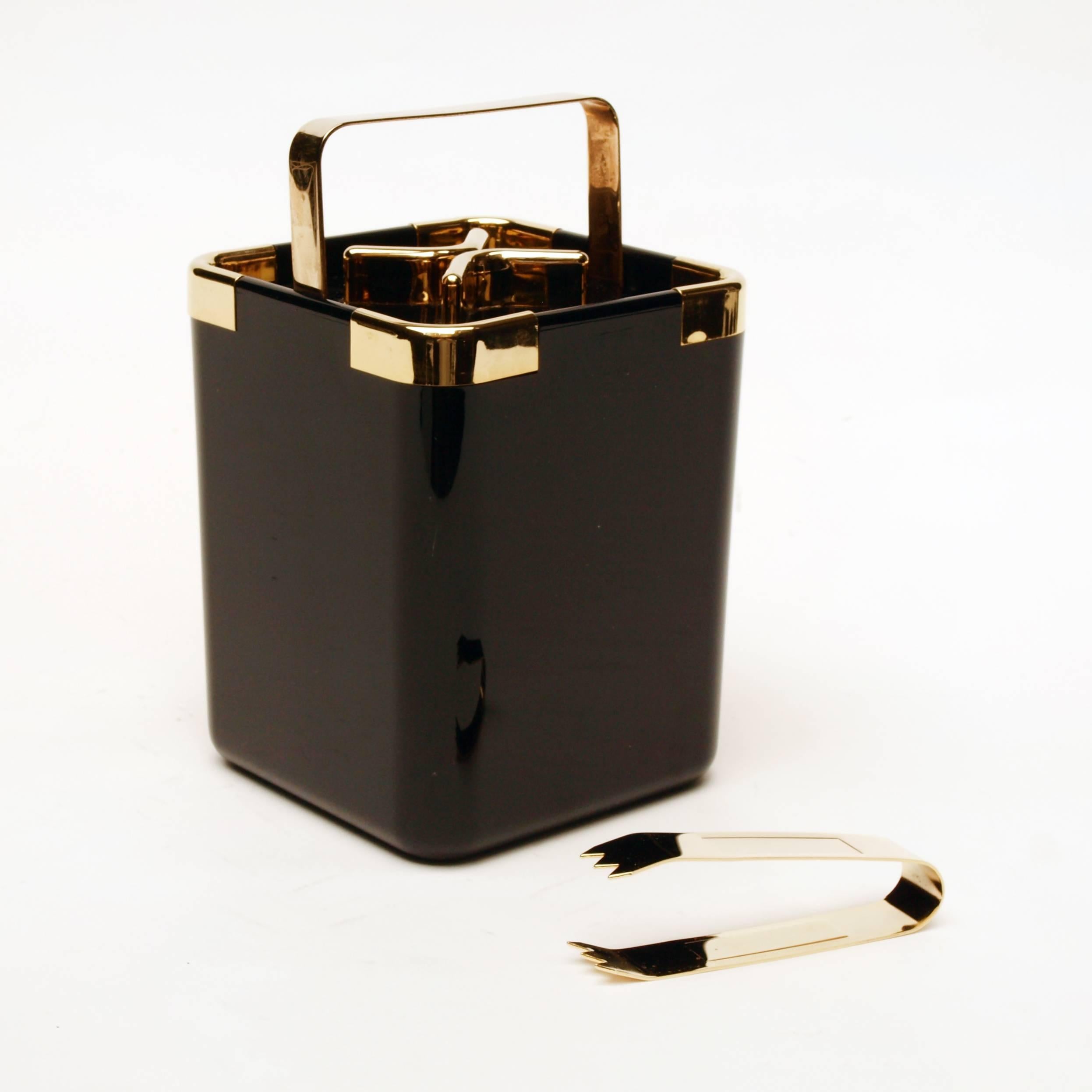 A glossy black and gold ice bucket dating from the late 1970s-early 1980s, with a folding brass handle and brass ice tongs. The condition is absolutely stunning as if never used. 

