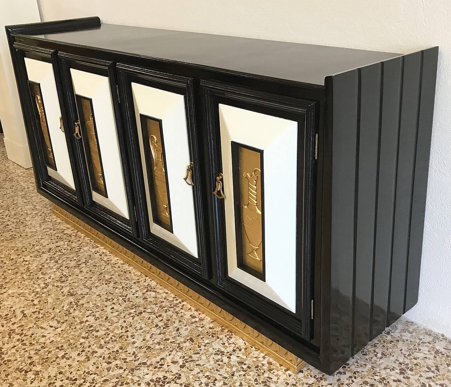 1940s Art Deco sideboard in ebonized oakwood with ivory lacquered details and gold-leafed solid wood engravings, the handles are made of brass and Bakelite.
On the inside of the four doors there are some shelves.
 