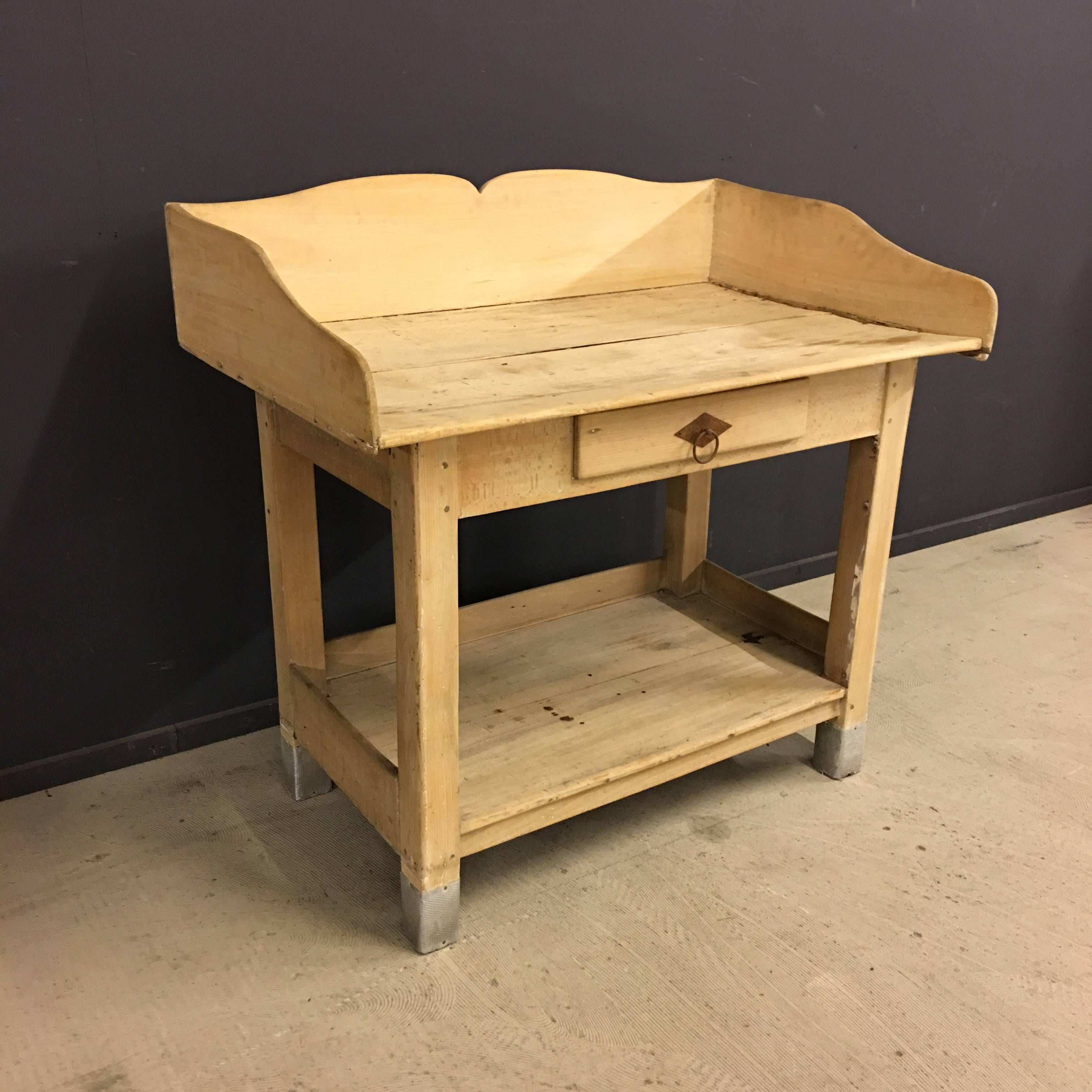 This French antique wooden baker table is manufactured during the 1920s and has been leached. The wooden top is slightly bended and has a worn look.
All four legs are covered with metal for protection.
It features one drawer.