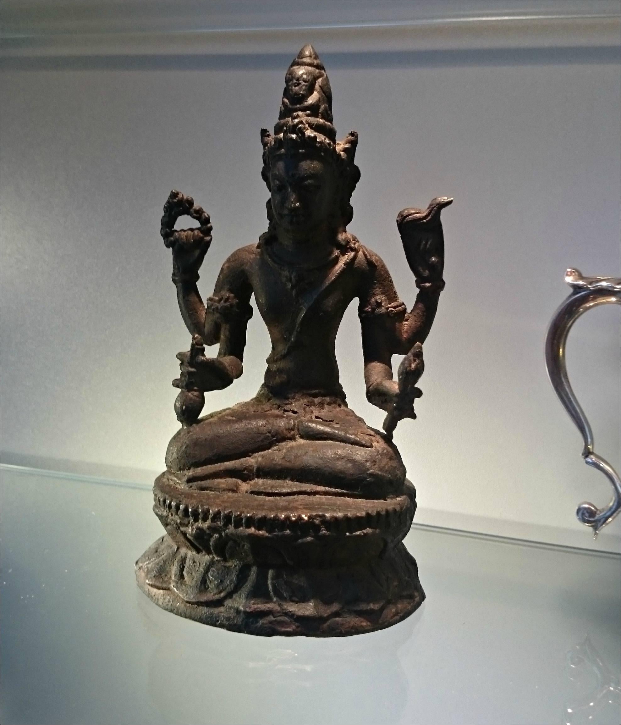 An early figure statue of Indian Shiva  
made of some cast metal may be bronze or iron.
The figure consist of four arms holding ritualistic objects, on a lotus shaped base.
    
   