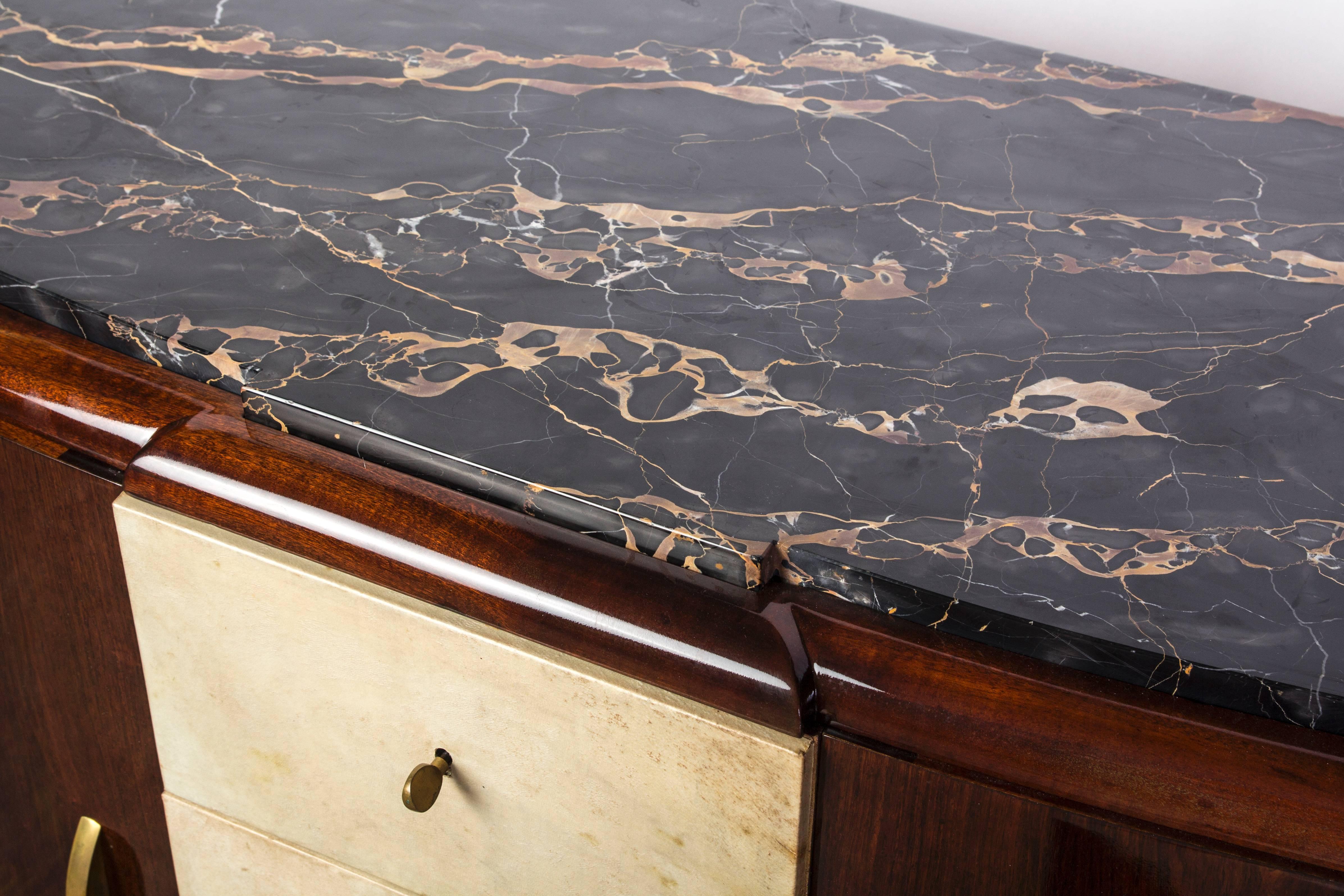 Elegant buffet Art Déco français en acajou signé par Maurice Rinck. Il se compose d'un plateau en marbre Portoro noir, de tiroirs au centre recouverts de parchemin et de portes d'angle arrondies avec quincaillerie en bronze.

Signature : E. Rinck