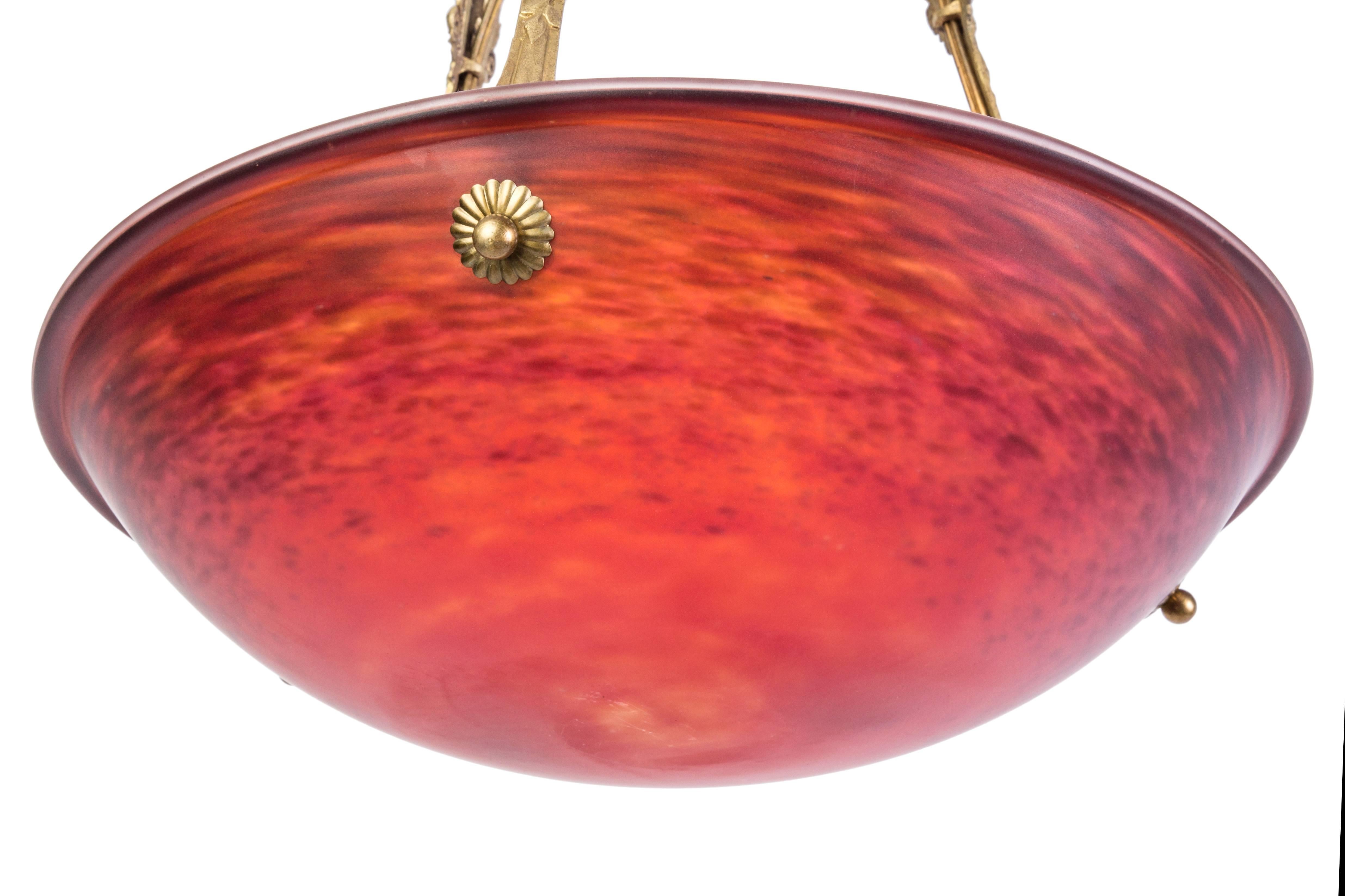 This exceptional 1920s French Art Deco chandelier features a beautiful crimson and sunflower colored glass shade, connected to an etched floral hand-wrought iron bronze frame. 

Made in France, circa 1920.