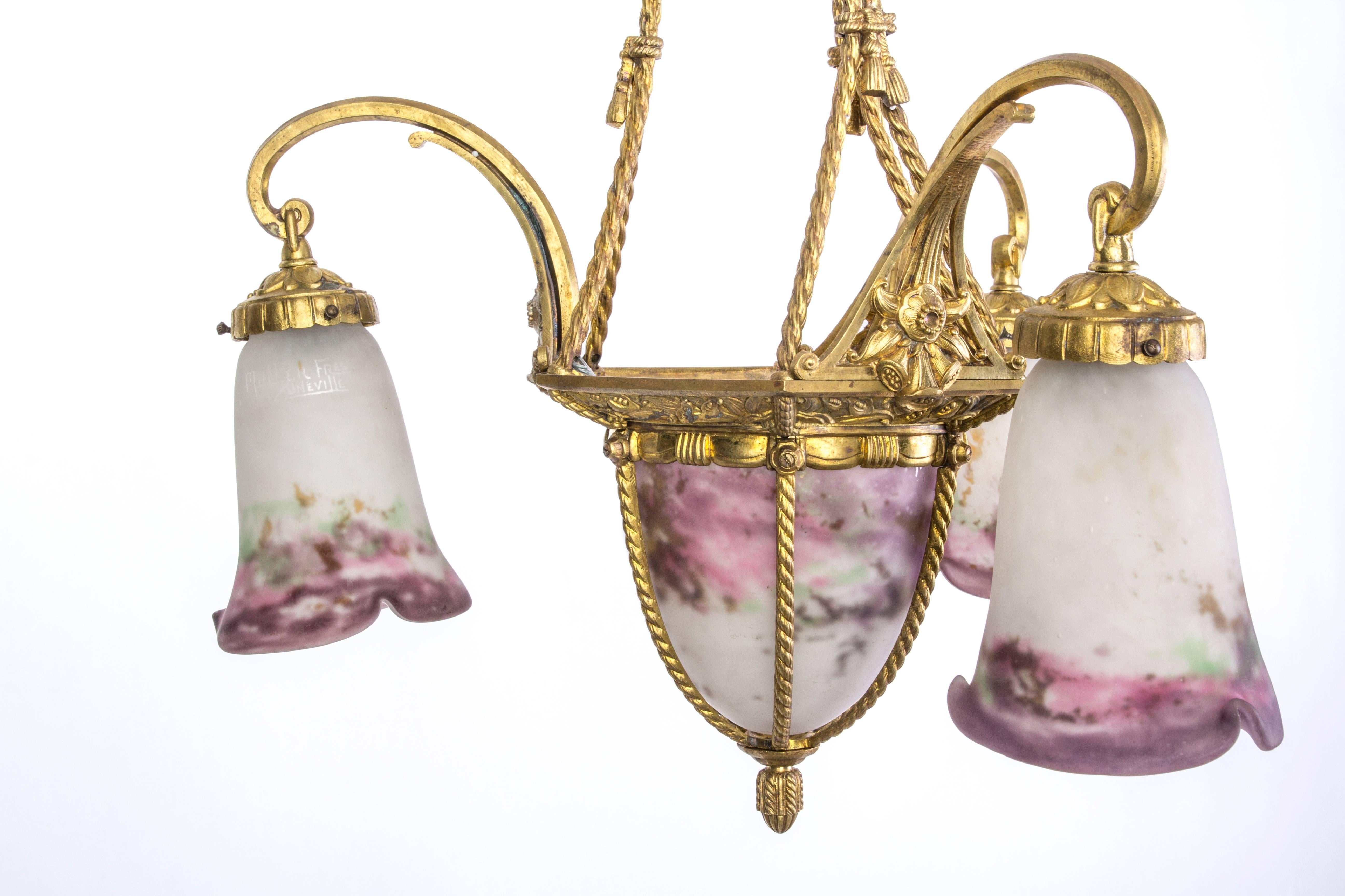 This sensational early French Art Deco chandelier was designed and signed by Muller Frères. It features a gilt bronze base in brass with stylized floral and chain detailing. It has an obus and (3) glass frosted glass shades with a painted floral