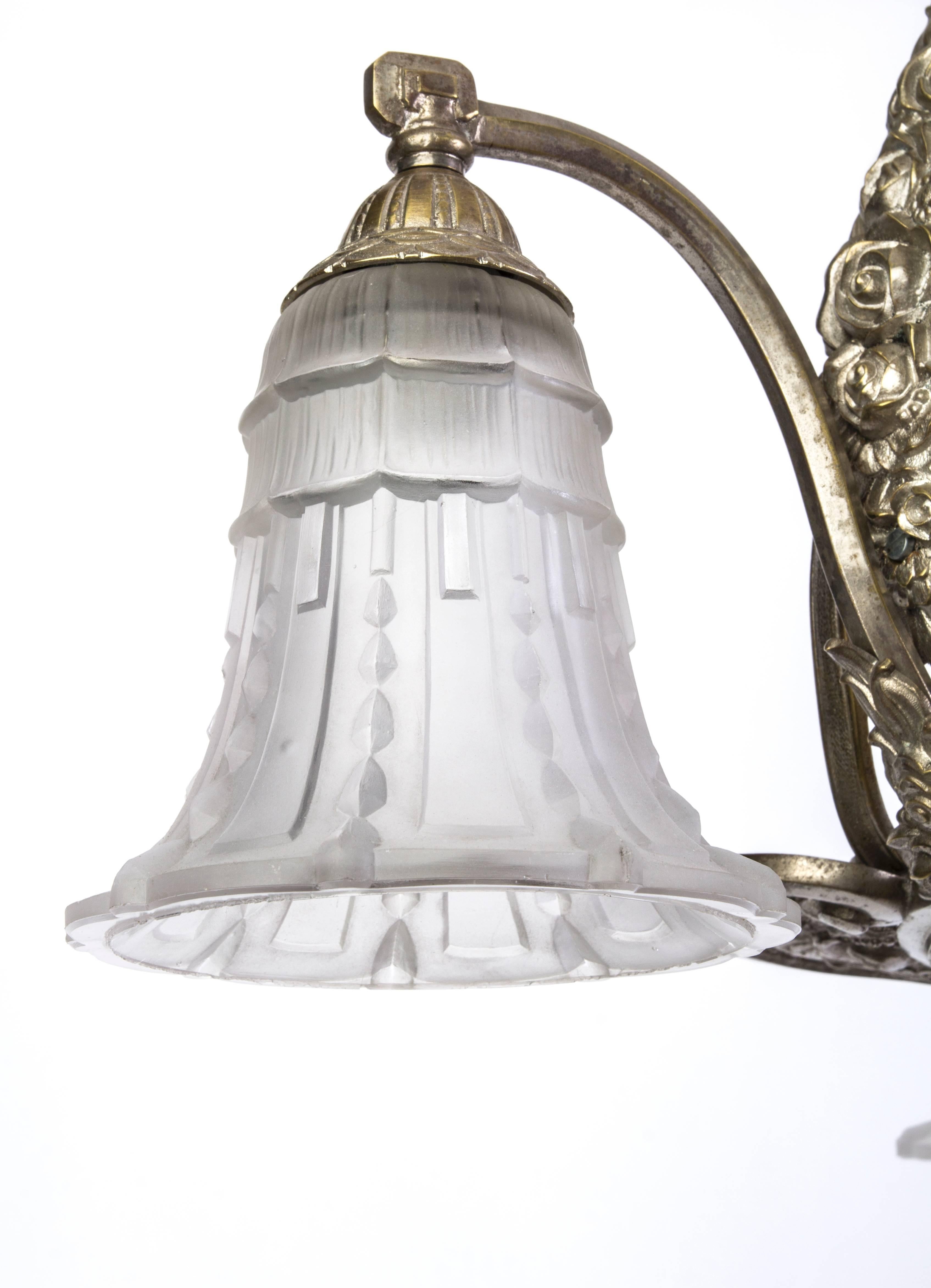 This stunning early French Art Deco chandelier features a nickel-plated bronze base with stylized floral detailing and relief frosted glass shades with geometrical motifs. It is in excellent condition.