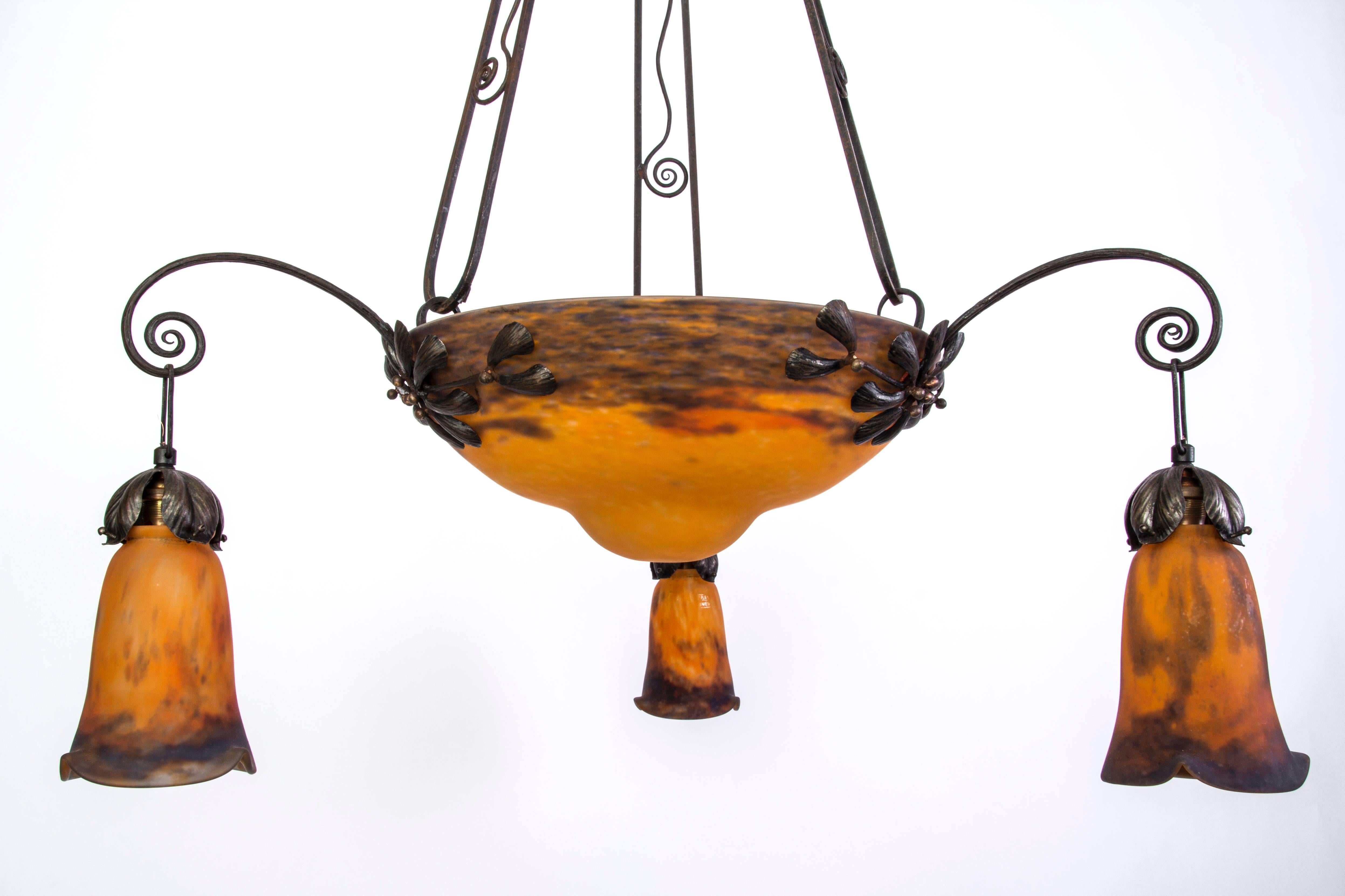 Original Art Deco chandelier from France made of wrought iron, beautifully designed and decorated. This piece is in excellent condition and features a large center bowl shade and three small shades, pâte de verre with marvellous inclusions, emitting