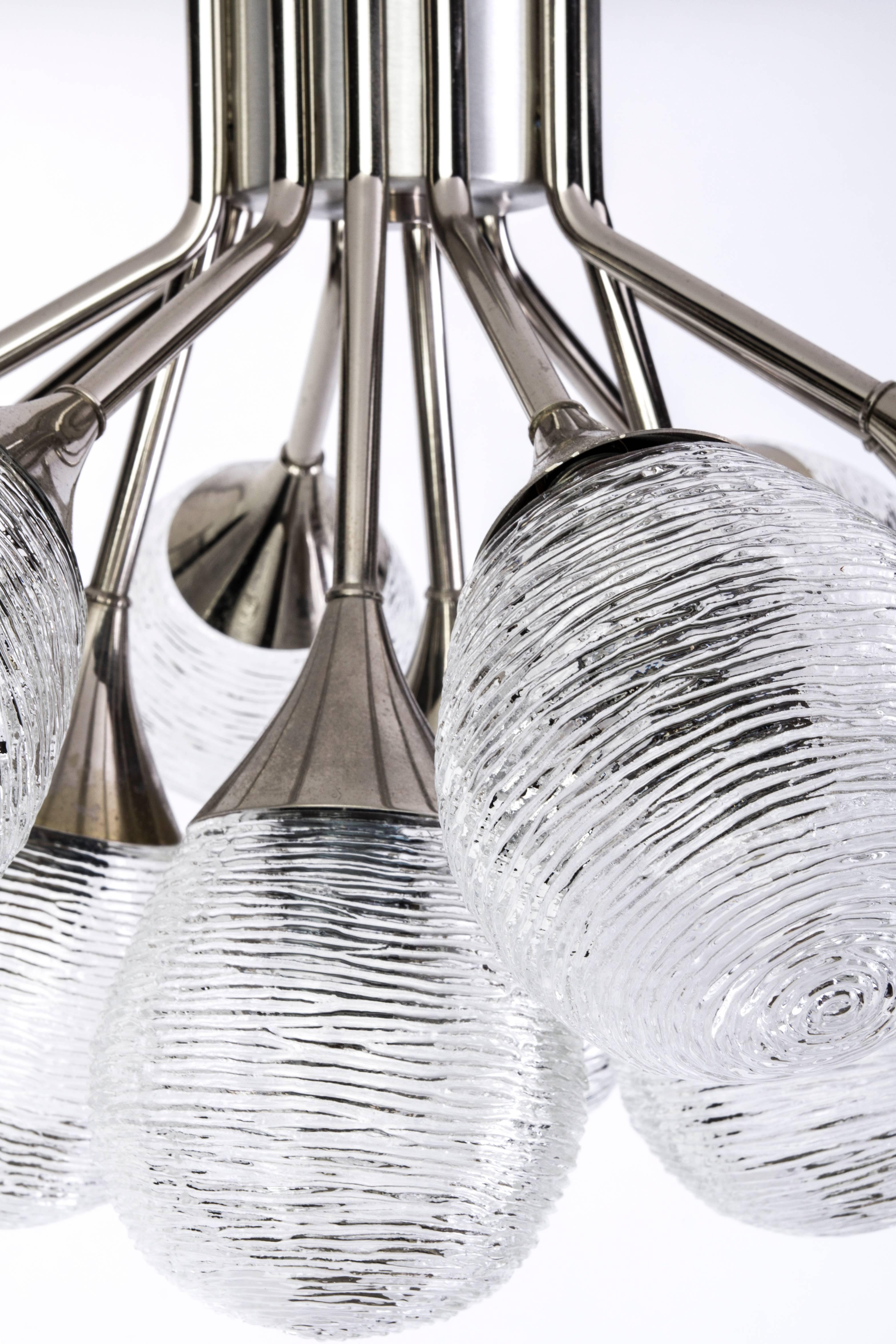 This luxe Mid-Century modernist Sputnik chandelier, features twelve (12) ribbed textured glass bulbs descending from a chrome frame creating a orbital form design.
 