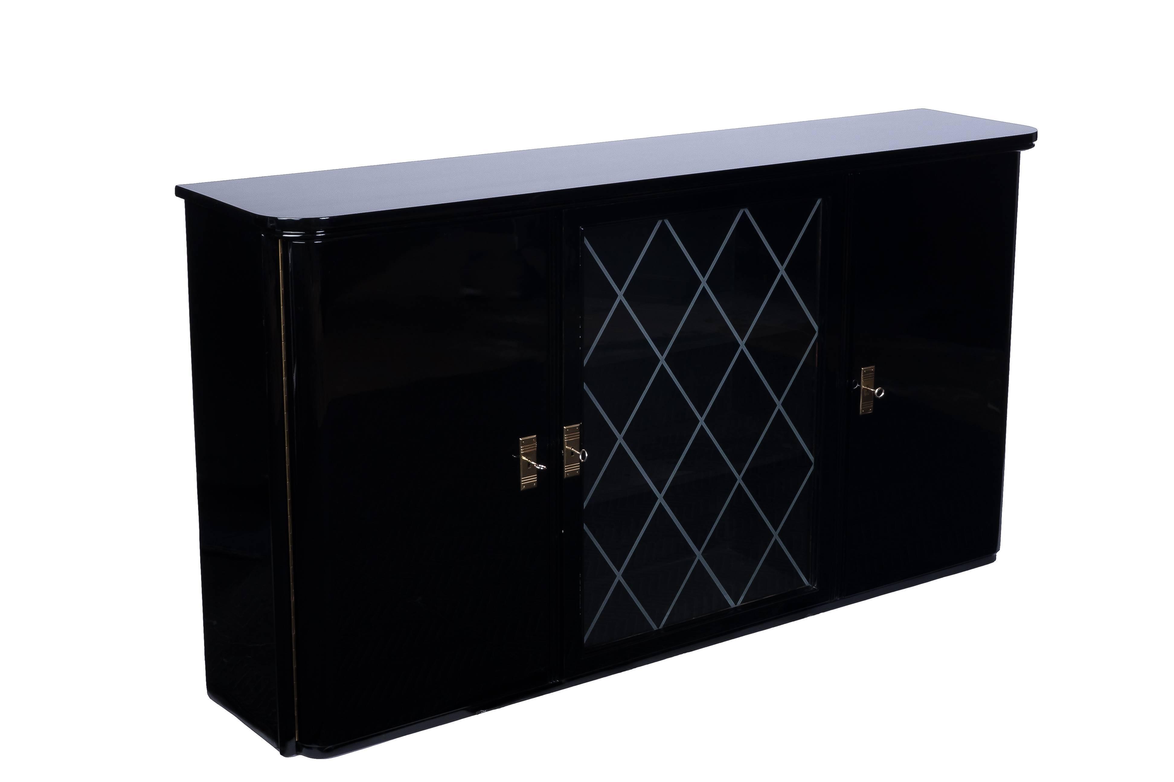 This gorgeous Art Deco high board features a rectangular form design with brass fittings finished in a beautiful high gloss black lacquer. The piece has two swing doors and a center etched glass door for display. Three drawers and shelves for plenty