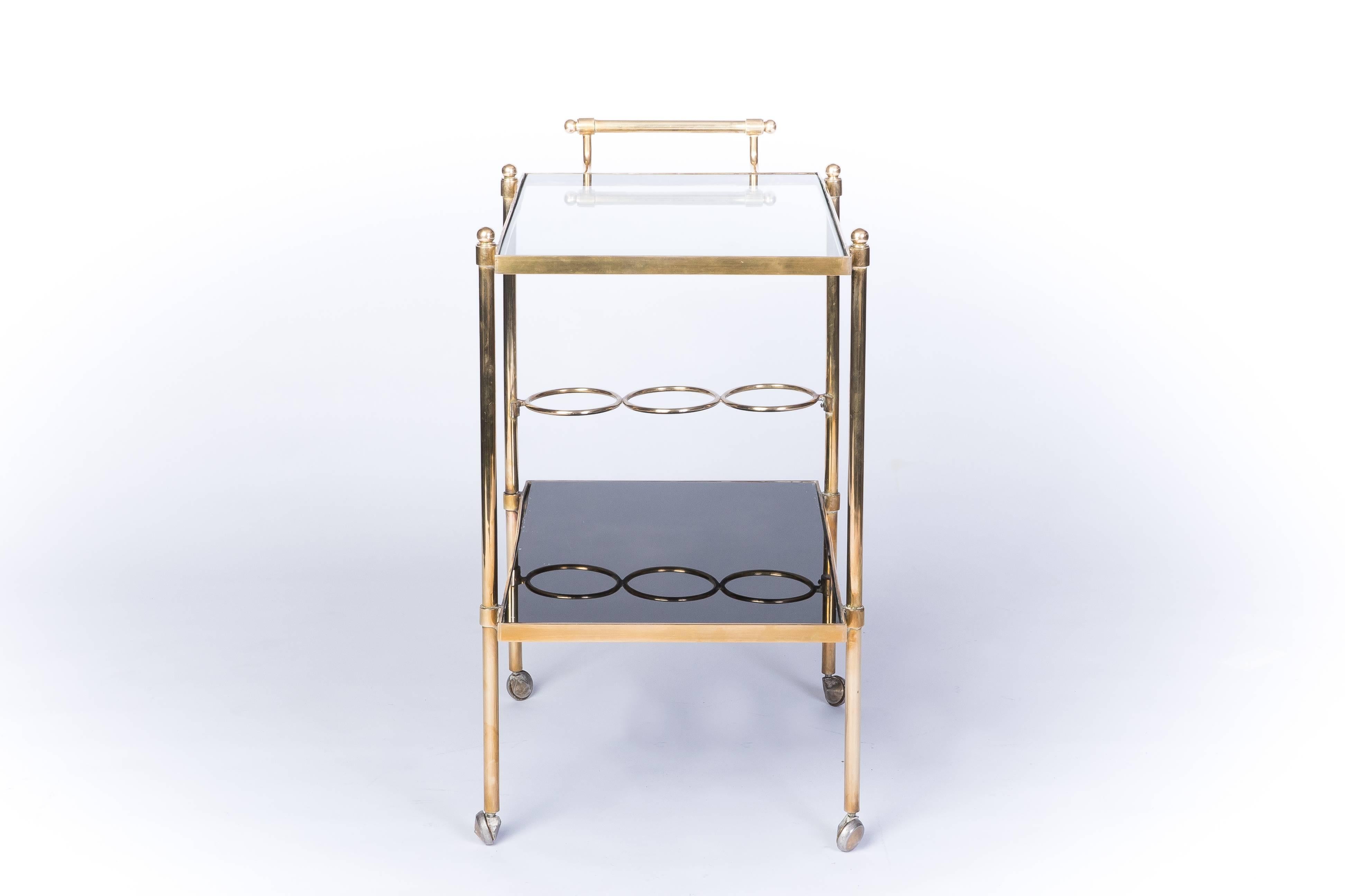 This stunning French Mid-Century Modernist bar cart (circa 1960) features a brass frame having with clear glass top and lower black mirror shelf with bottle holders.