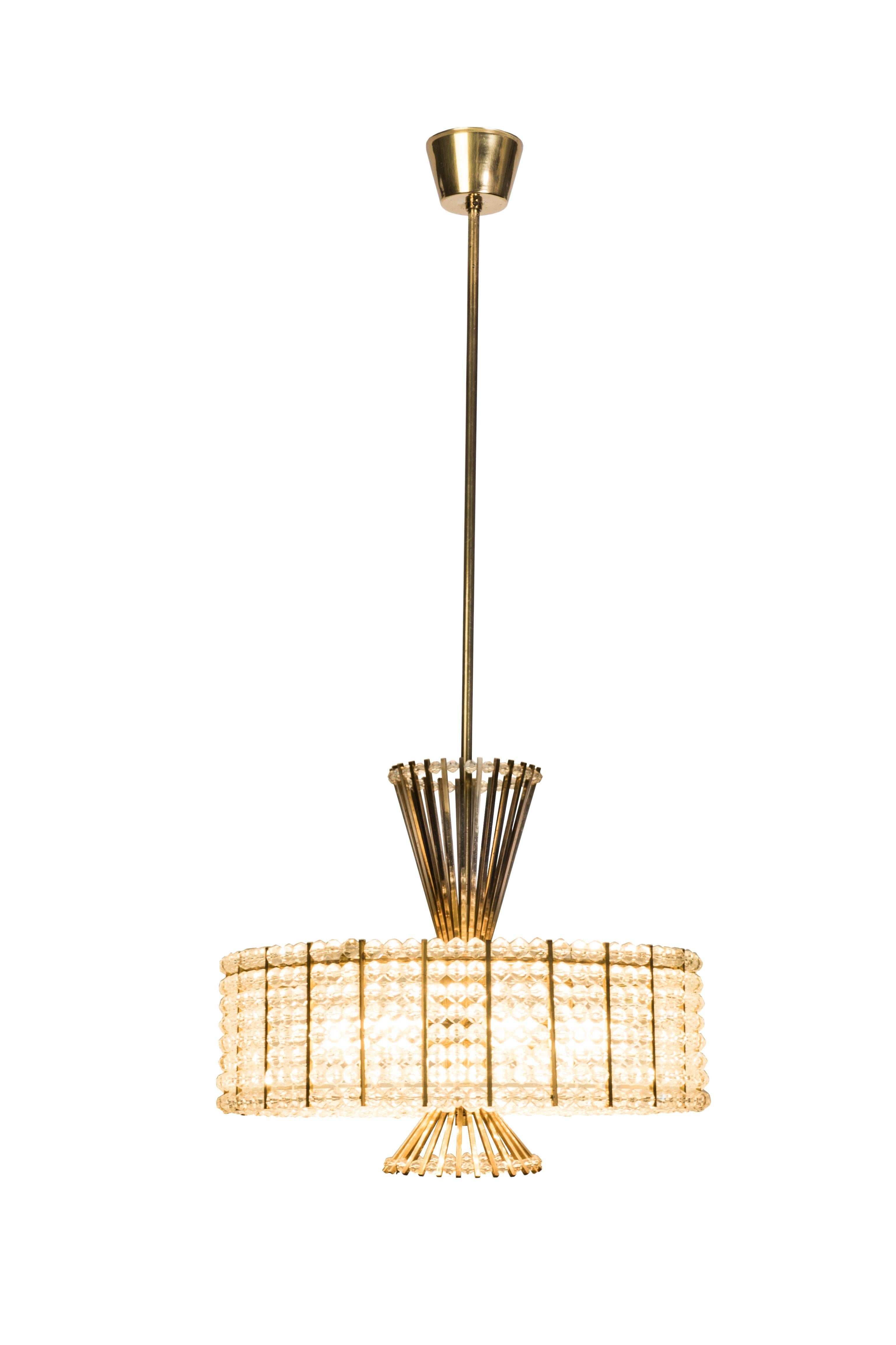 This sensational Mid-Century Modernist chandelier was designed by Emil Stejnar For Rupert Nikoll. It features a circular drum of Lucite and acrylic chain detailing connected to a brass base with conical form lines protruding from the top and bottom