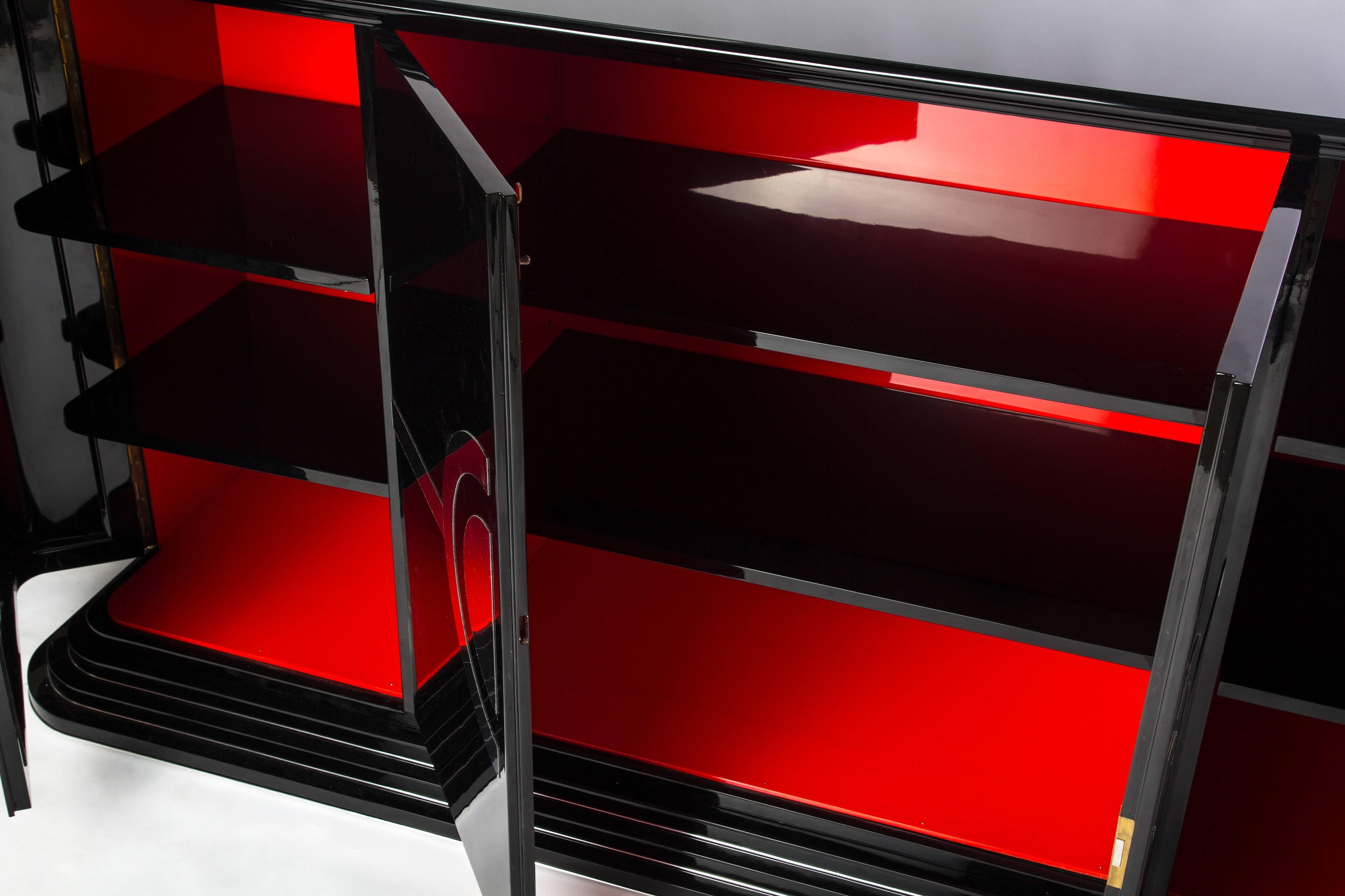 Luxurious Art Deco sideboard features a high gloss black lacquer finish with a cascading stair foot, three swing doors, chrome lines and fixtures, and a luscious cherry interior.