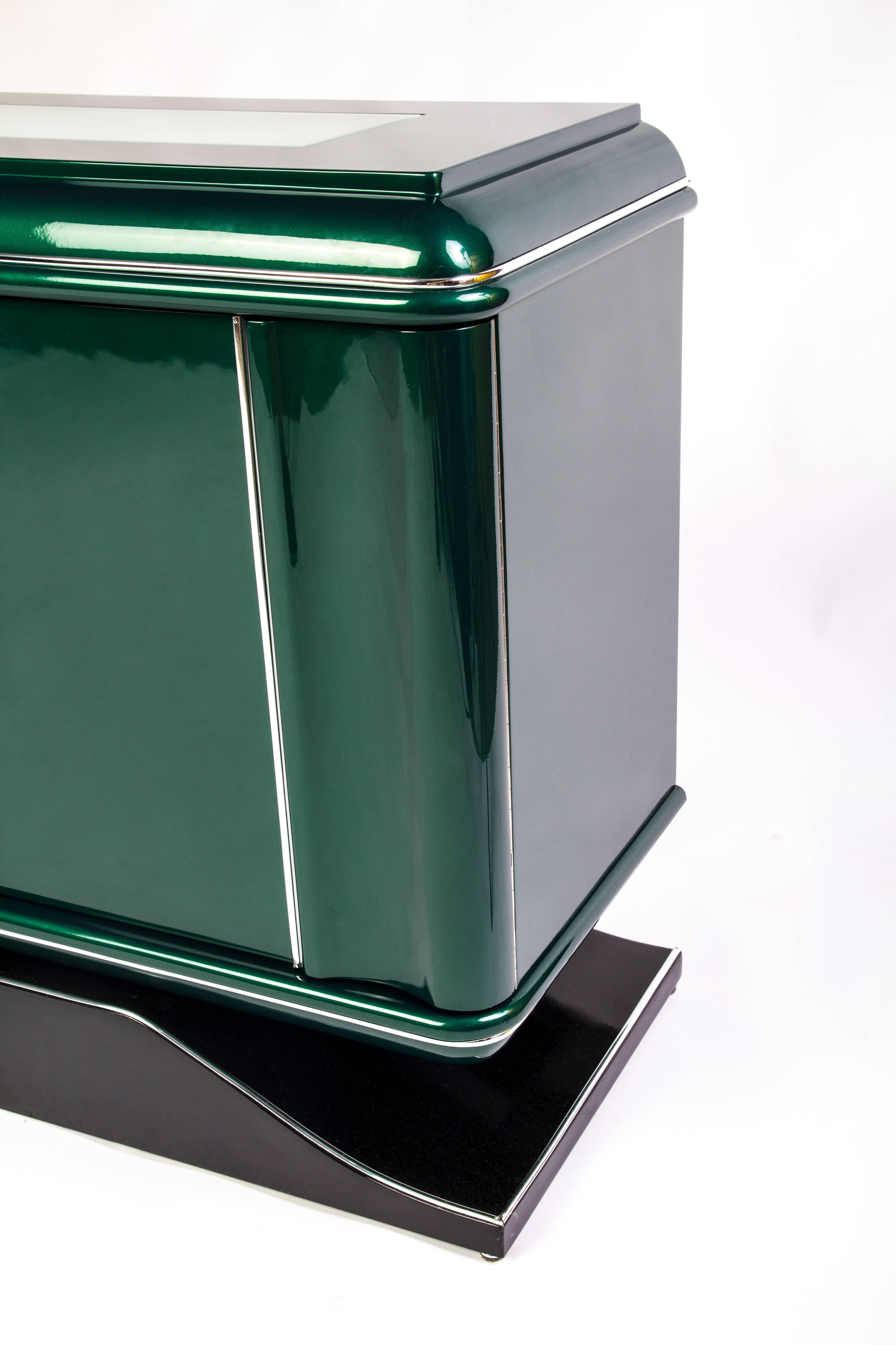 This extraordinary Art Deco commode features a built in translucent light that reflects on the top and interior of this piece, with an evergreen high gloss lacquer finish. It has a French foot base with chrome lines and fixtures, finished in a high