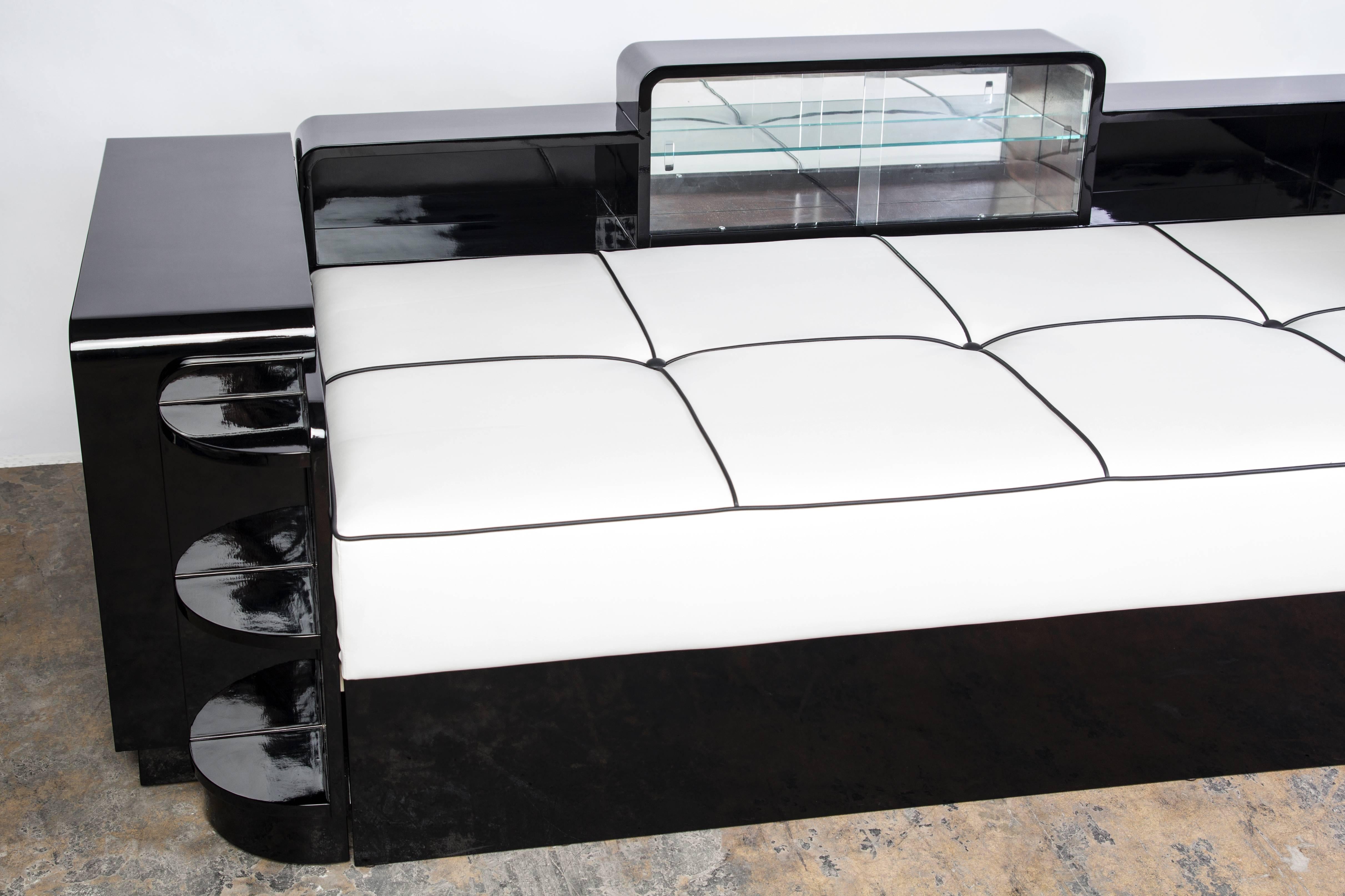 This magnificent French Art Deco daybed features an streamline design in high gloss black piano lacquer and covered with a luscious leather upholstered cushion. The piece features a display compartment with mirror back and glass shelve and doors.