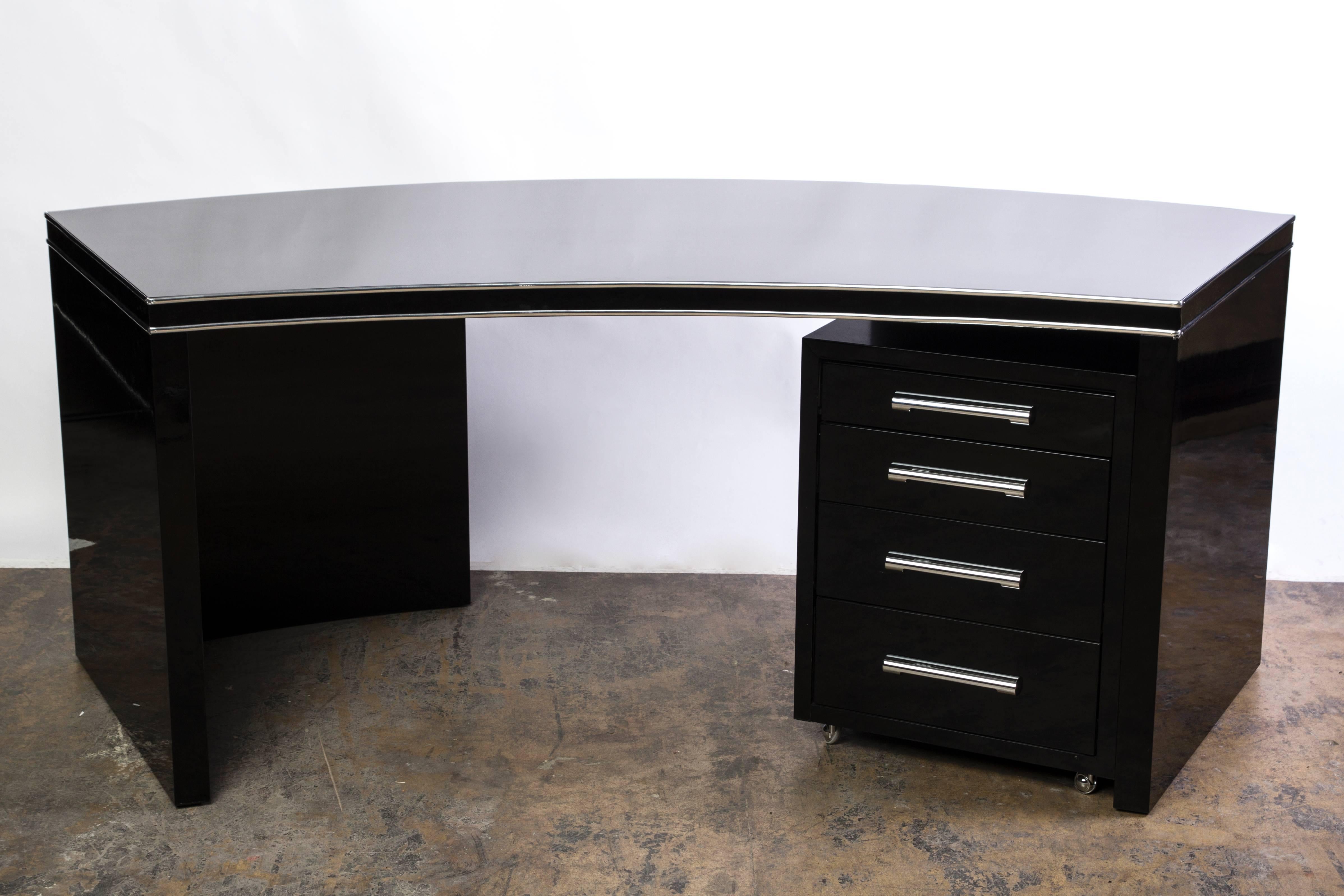 This wonderful Art Deco desk features a curved design with chrome-line embellishments and finished in a high gloss black lacquer and chrome finishes. The pieces comes accompanied by a filing cabinet with four (4) drawers.

