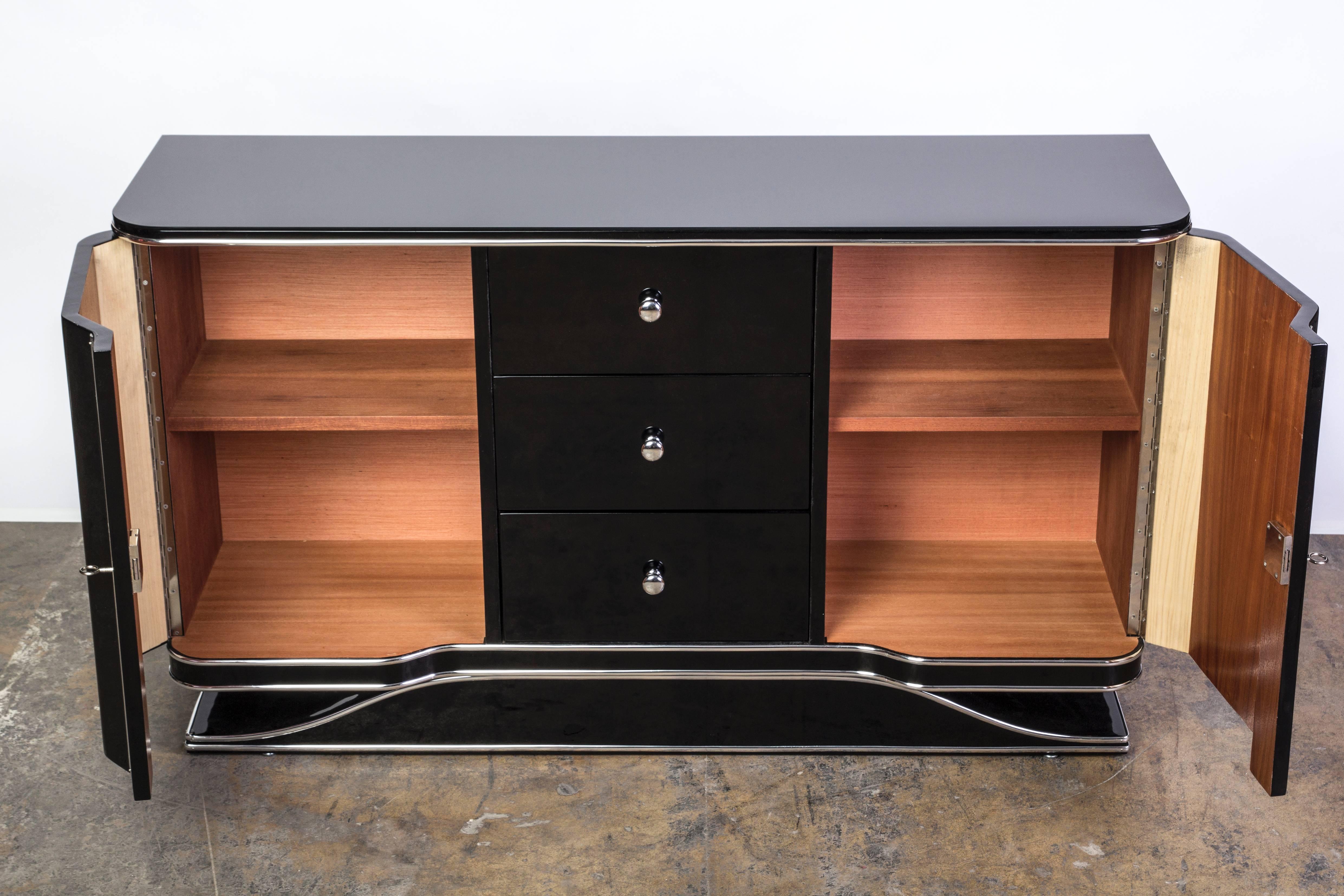 This beautiful Art Deco sideboard or credenza features two (2) curved doors, three (3) center drawers and chrome fittings and fixtures, finished in a high gloss black lacquer.