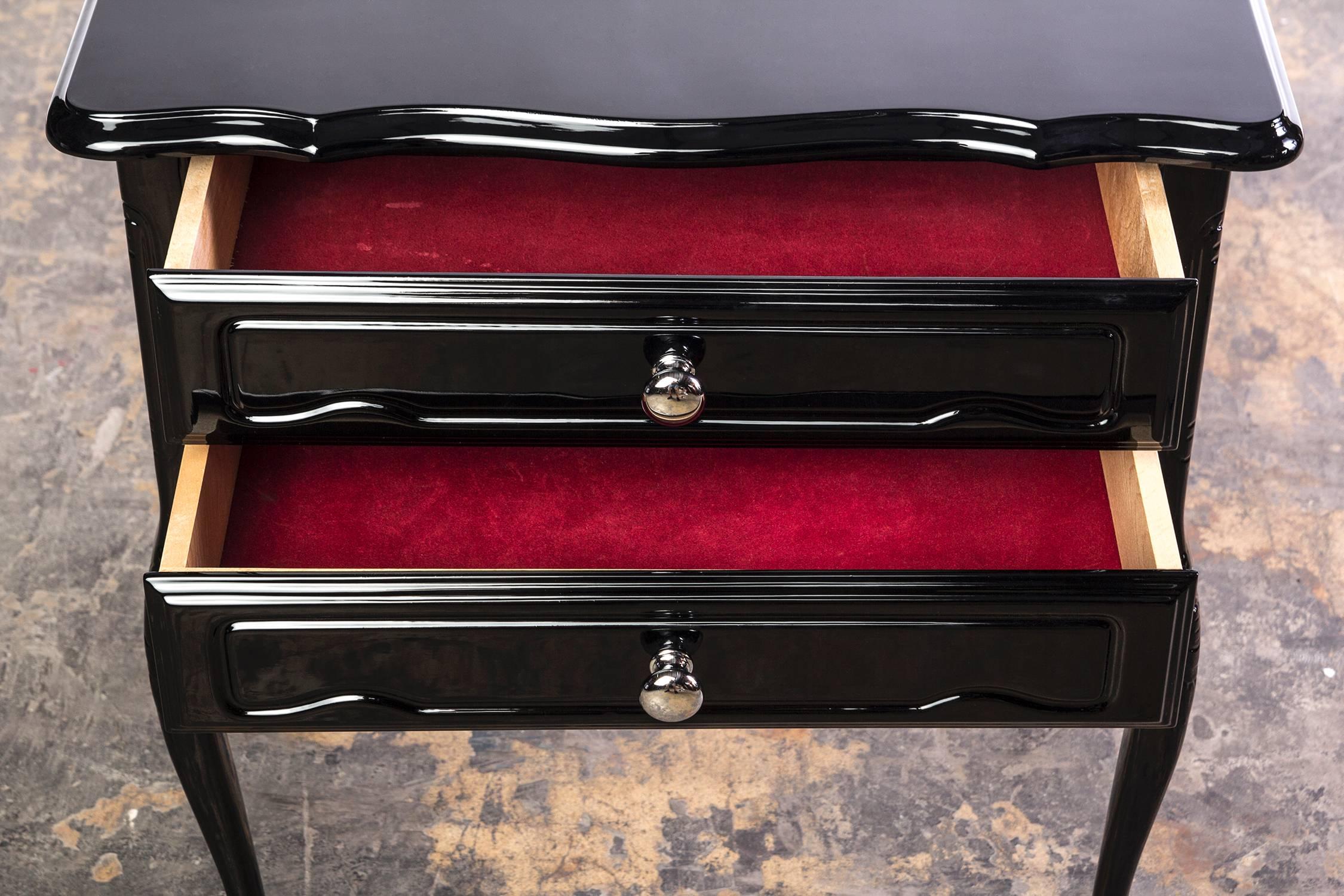 Cette chic table d'appoint ou de bout Art Déco française comporte deux tiroirs avec des poignées chromées, des pieds incurvés et une finition en laque noire brillante. Intérieur des tiroirs doublé en velours Vin de Rouge.