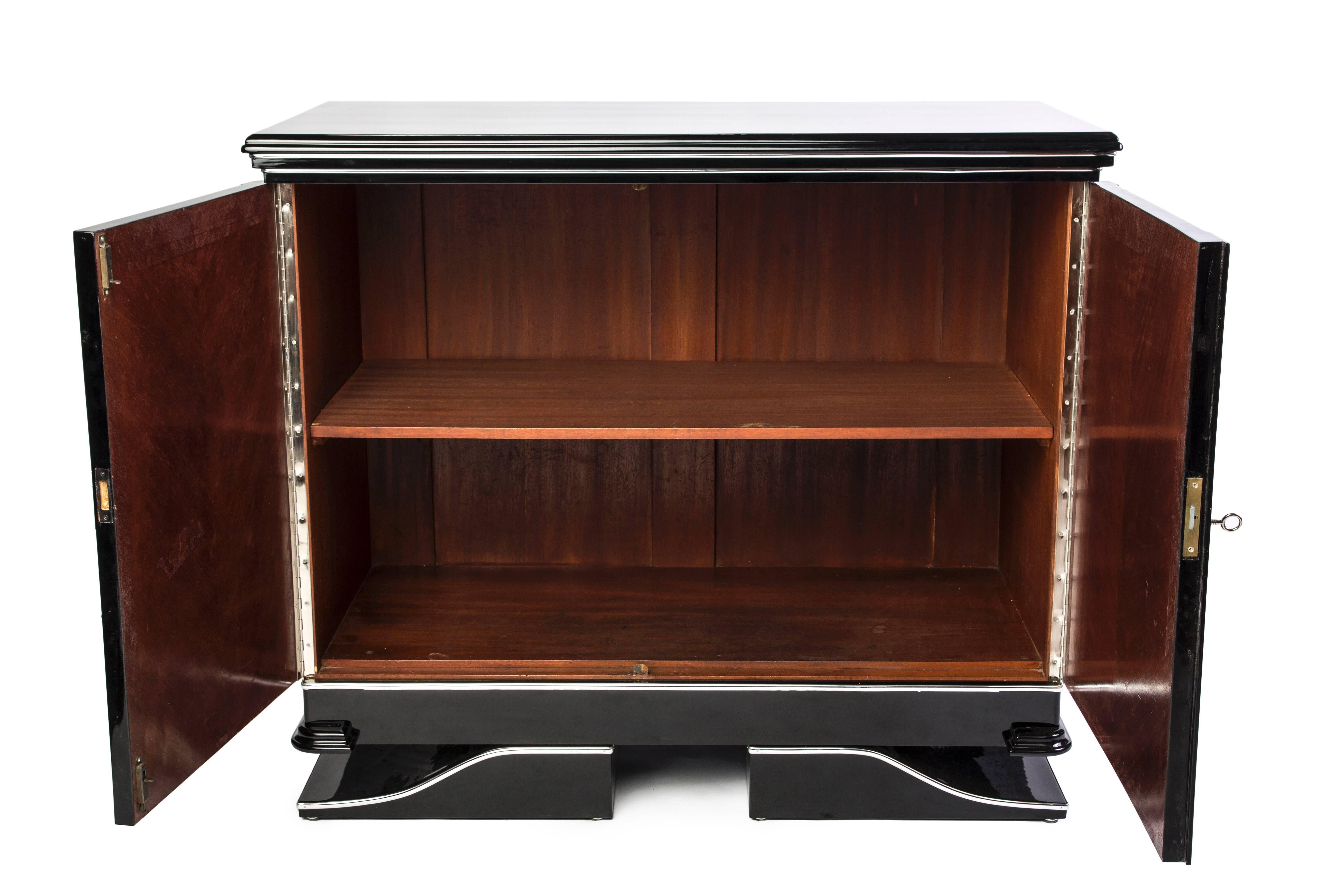 This elegant Art Deco commode features chrome lines applications and a cherrywood interior with a black piano lacquer finish.