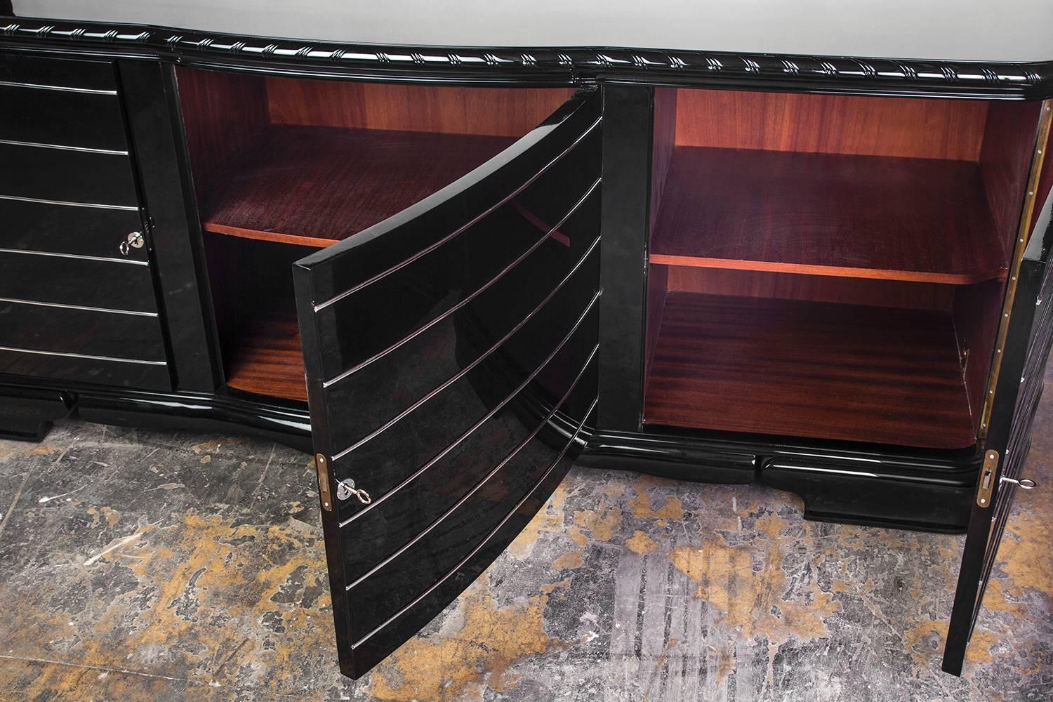 This exceptional streamlined Art Deco sideboard by ZKWAMZ, features a beautiful high gloss black lacquer with a curved body, chromed fittings and fixtures. The piece depicts mahogany interiors. The piece is model Wuppertal Bufett