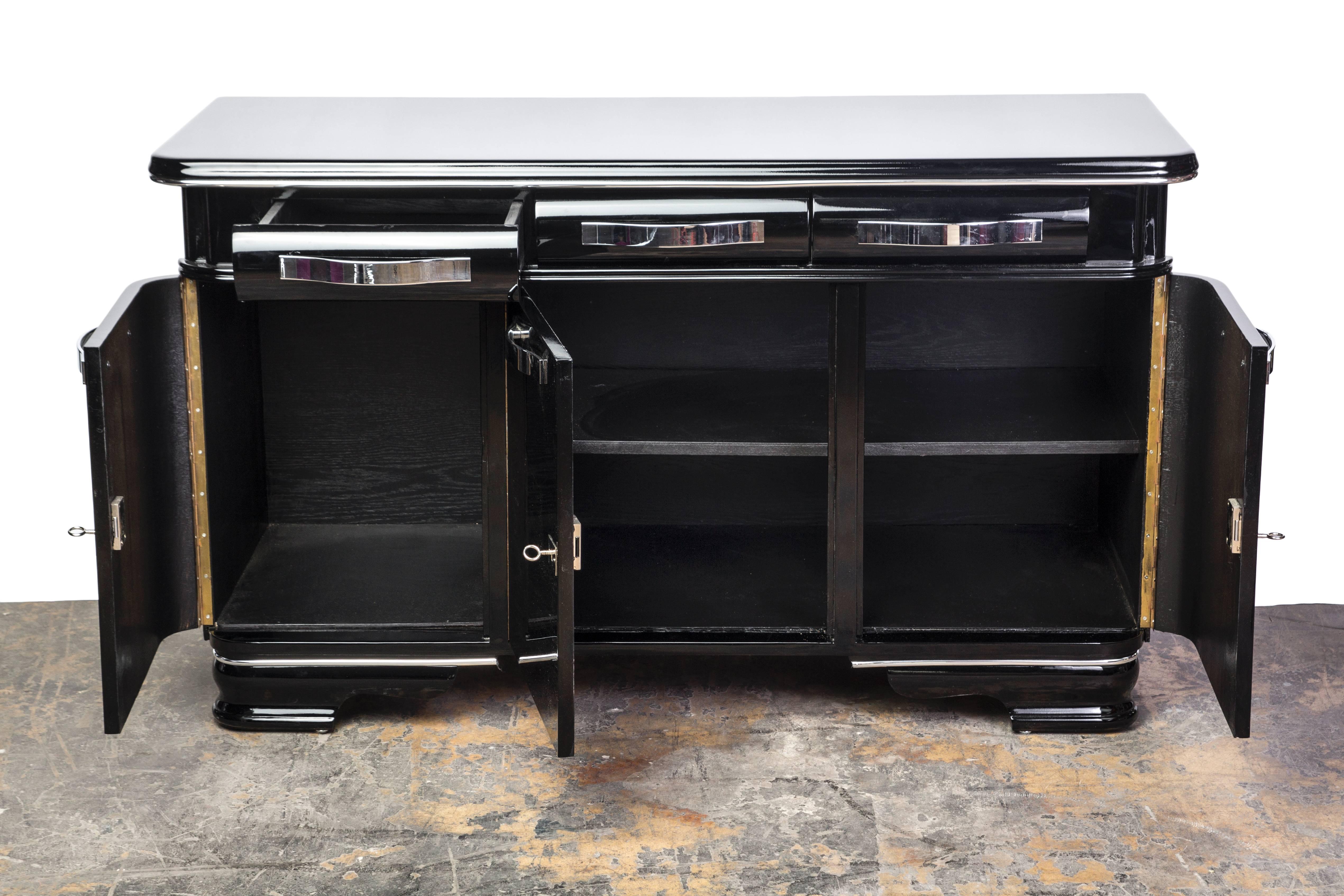 This unique sideboard from Mons features a streamline design with plenty of storage and striking beauty. The piece has been fully refinished in a black piano-lacquer exterior and matte black interior. It has three swing doors, chromed hardware and