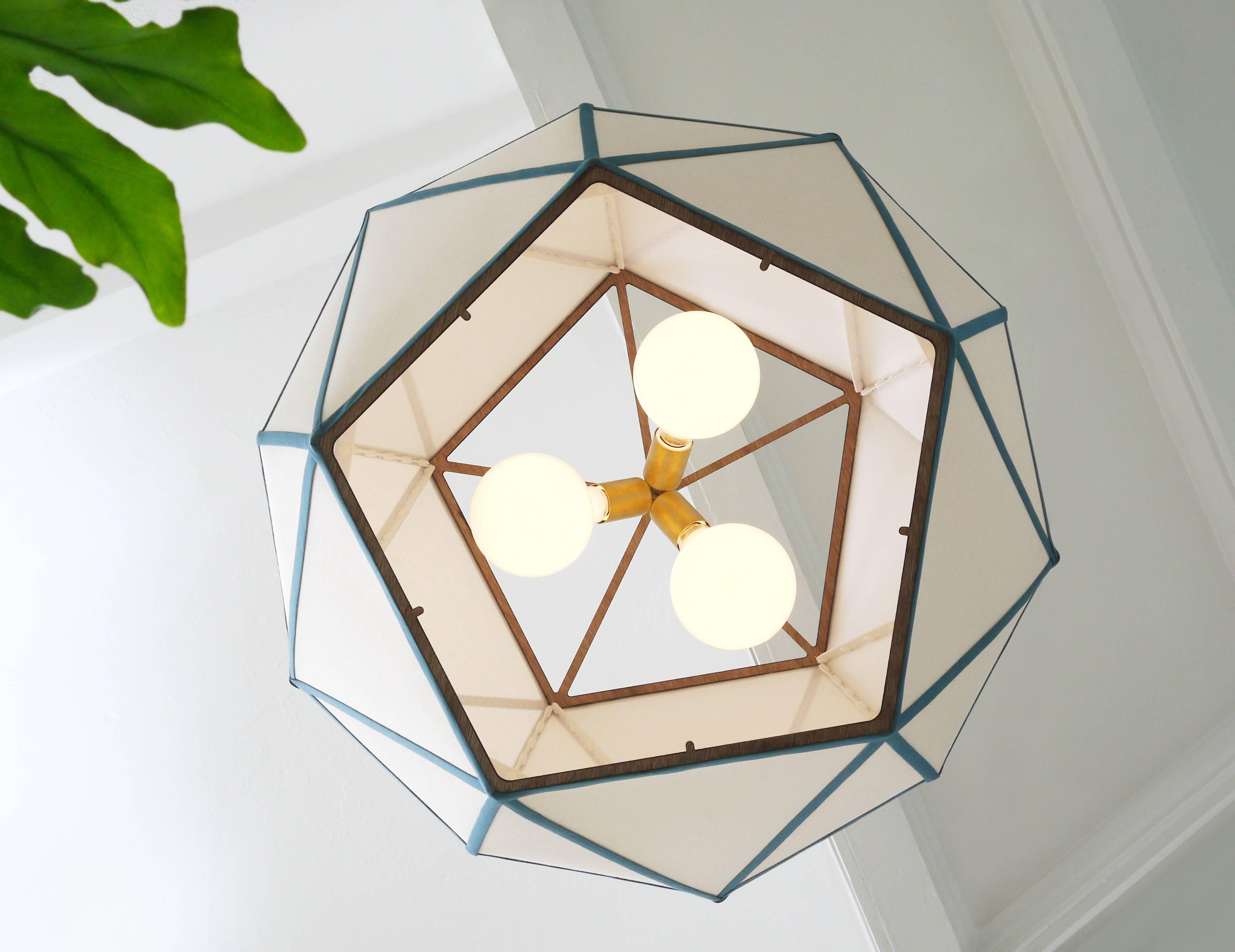 Crisp geometric forms rendered in hand riveted die-cut linen, laser cut plywood and brushed brass.

Features three 60 watt incandescent lightbulbs and an included optional diffuser.

Available in six standard trims. Shown here in ocean.