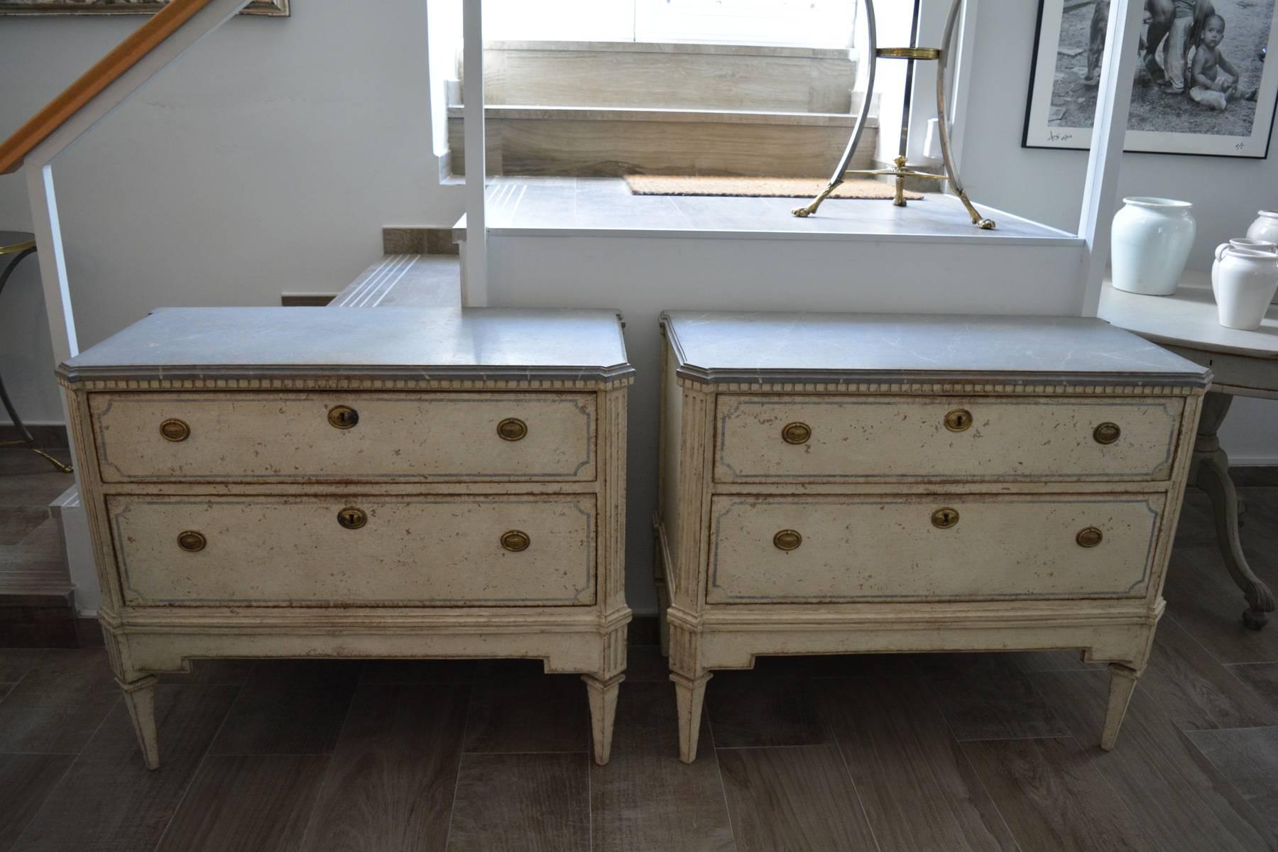 A pair of Gustavian Style chest of drawers in antique white color with light grey top imitating marble. They keep the original locks and hardware, 
circa 1860.