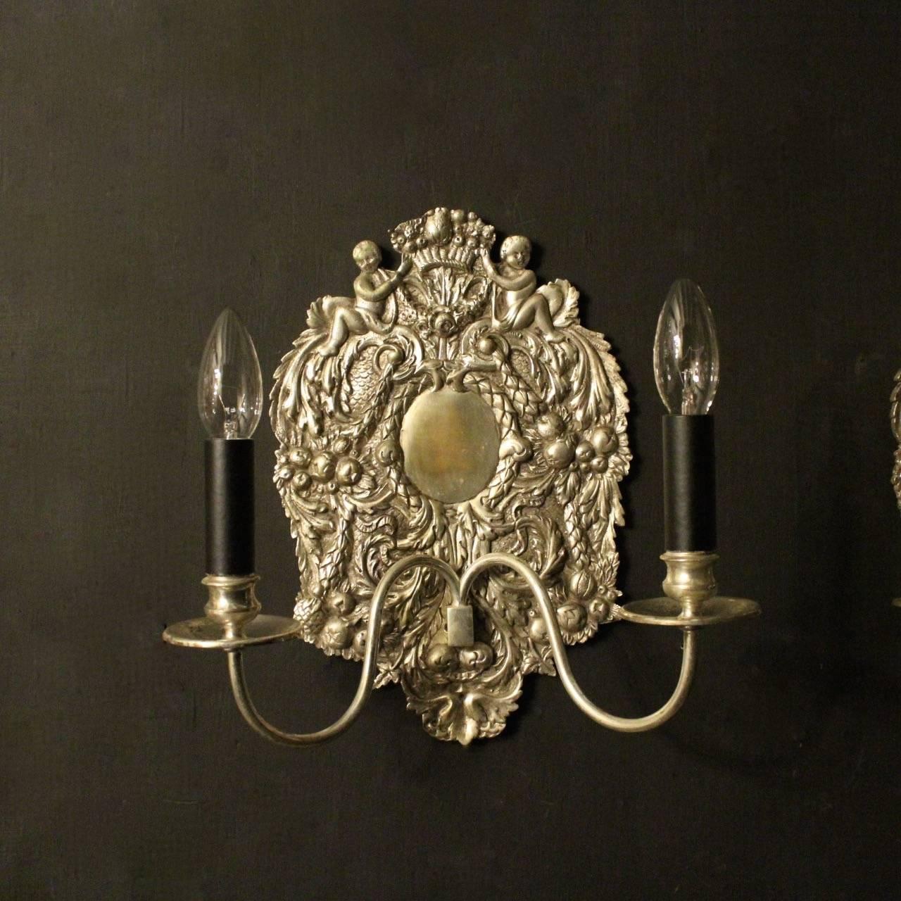 English set of four twin arm silvered cast brass antique wall lights, the scrolling arms with circular cast drip pans and turned candle sconces, issuing from foliated leaf and grape backplate with an ornate finial of a pair of cherubs holding a
