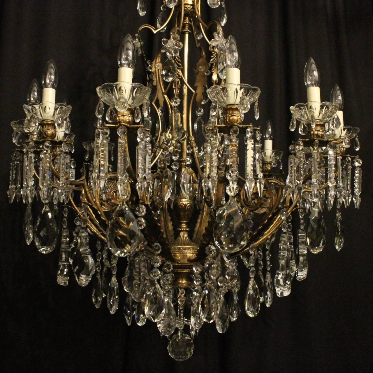 A French gilded cast bronze and crystal twelve-light cage form antique chandelier, the acanthus leaf scrolling arms with glass bobeche drip pans and leaf candle sconces, issuing from an foliated pierced cage form interior, decorated overall with