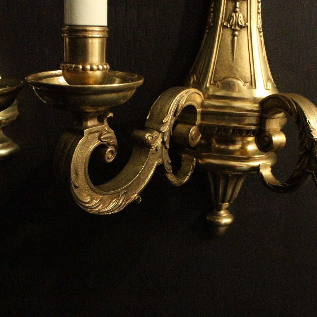 A French pair of bronze twin branch antique wall lights in the Louis XIV taste, the scrolling leaf square gauge scrolling arms with circular bobeche drip pans and millgrain candle sconces, issuing from a foliate moulded back plate with decorative