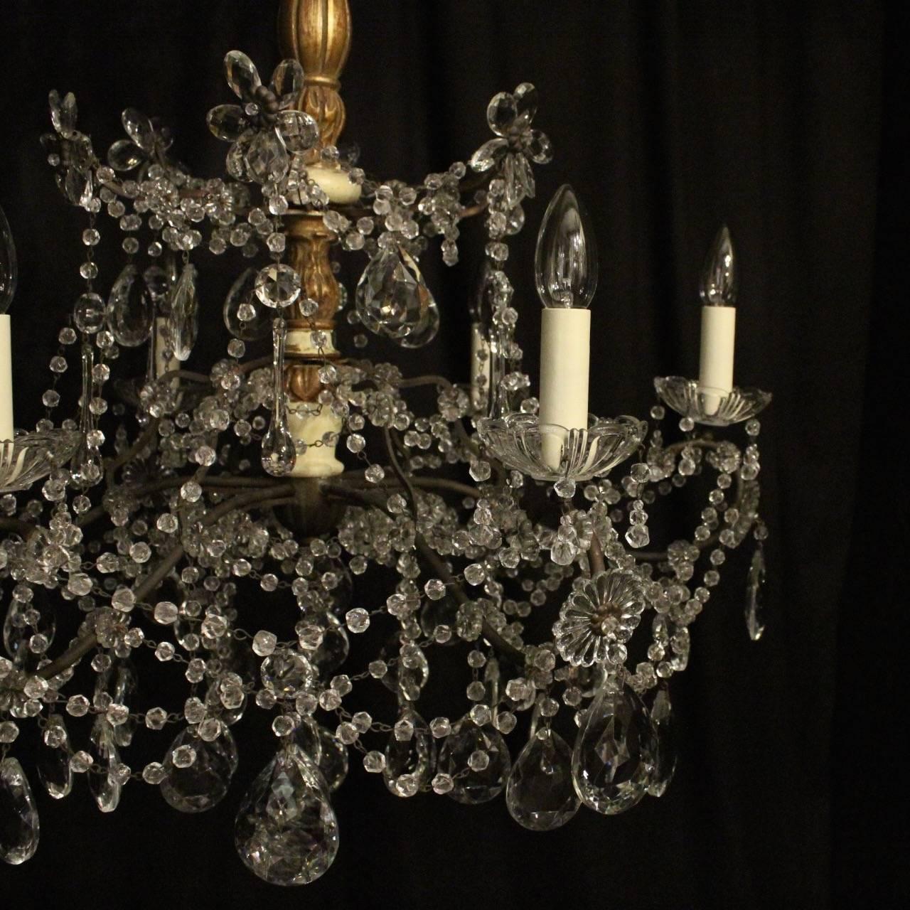 An Italian Florentine giltwood and crystal six-light antique chandelier, the oxidized brass scrolling arms with glass bobeche drip pans, issuing from an ornate carved giltwood central column with ornate scrolling canopy, decorated overall with