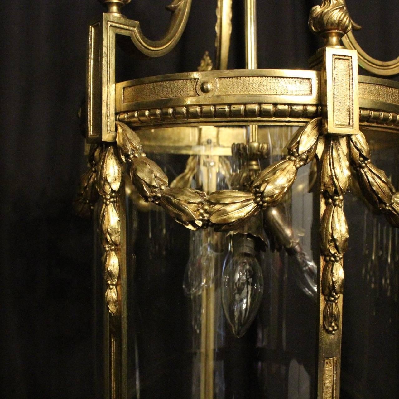 Quality French gilded bronze triple-light antique lantern, the six convex shaped glass panels held within an ornate scrolling framework, having three light fittings with a reeded central column, the bronze frame having decorative Floral swaged
